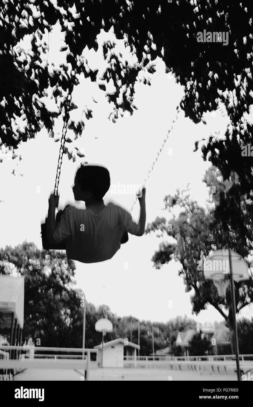 Blurred Motion de garçon bénéficiant sur Swing en aire de jeux Banque D'Images