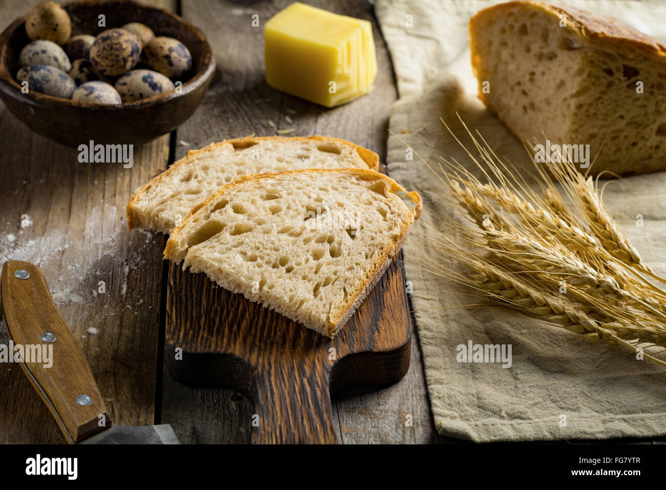 Pain au levain, morceau de fromage, œufs de caille, les épis de blé d'or et le couteau sur la table en bois rustique. La nourriture rustique still life Banque D'Images