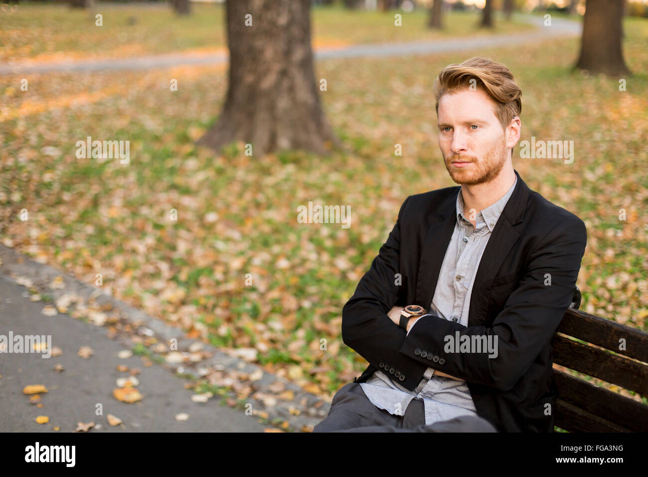 Jeune homme sur un banc de parc à l'automne Banque D'Images