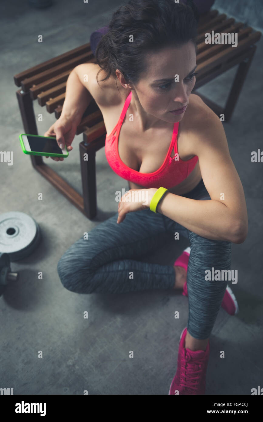 Le corps et l'esprit de l'exercice dans loft studio de remise en forme. Woman sitting in Fitness Gym loft with cell phone Banque D'Images
