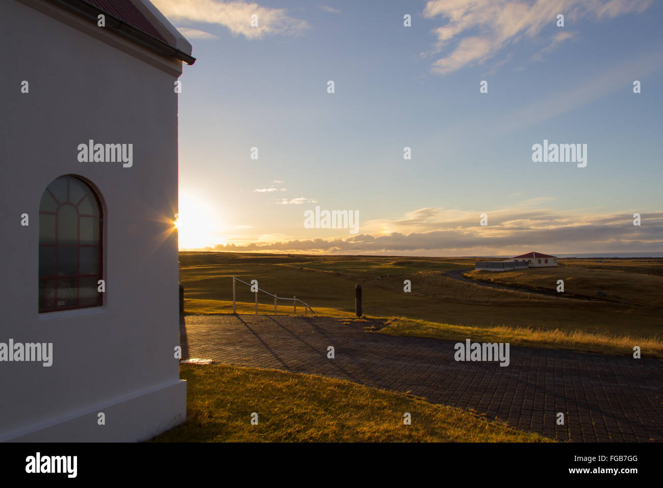 Un coucher du soleil tombe derrière une église blanche dans la péninsule de Snæfellsnes, l'Islande, avec des champs verts et ciel bleu en arrière-plan Banque D'Images