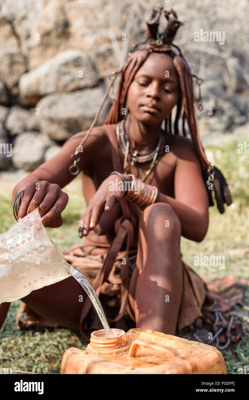 Femme Himba la collecte de l'eau dans un récipient de plastique à partir d'une source naturelle. Banque D'Images
