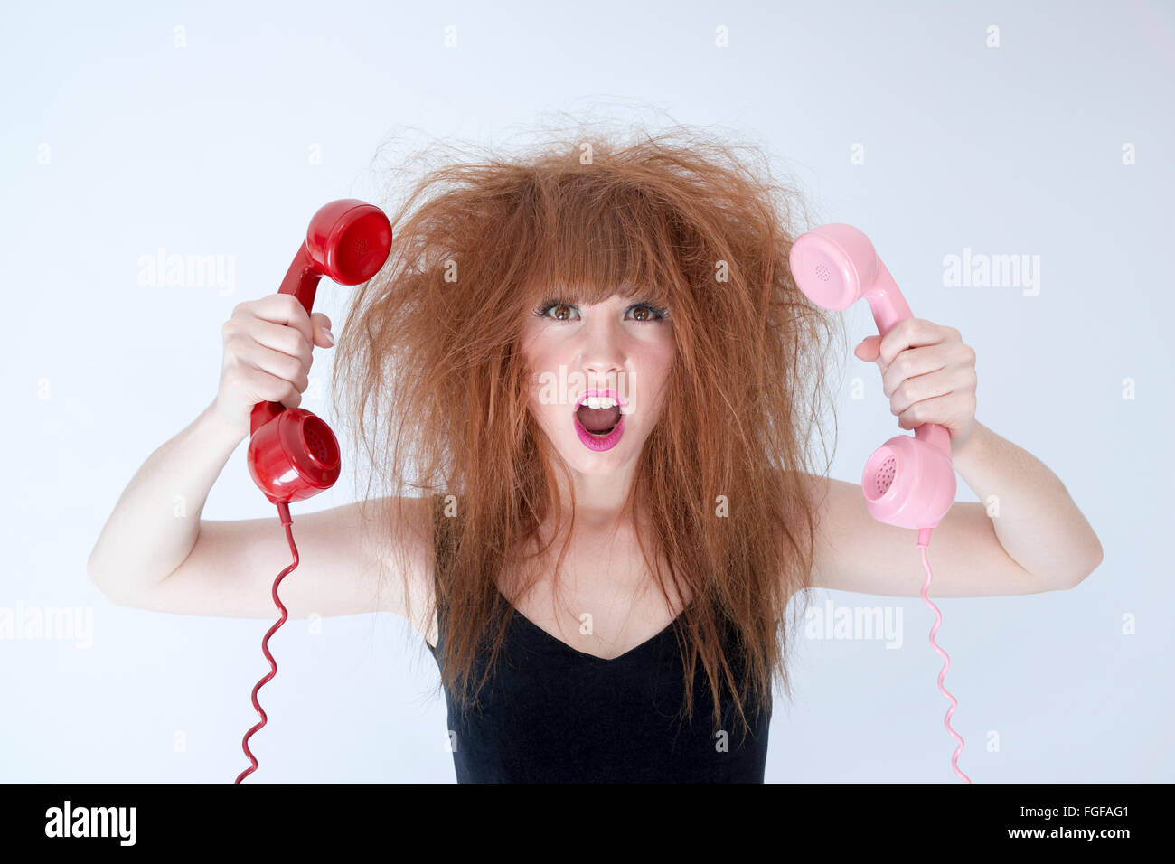 Femme aux cheveux en désordre tenant deux cris téléphones rétro Banque D'Images