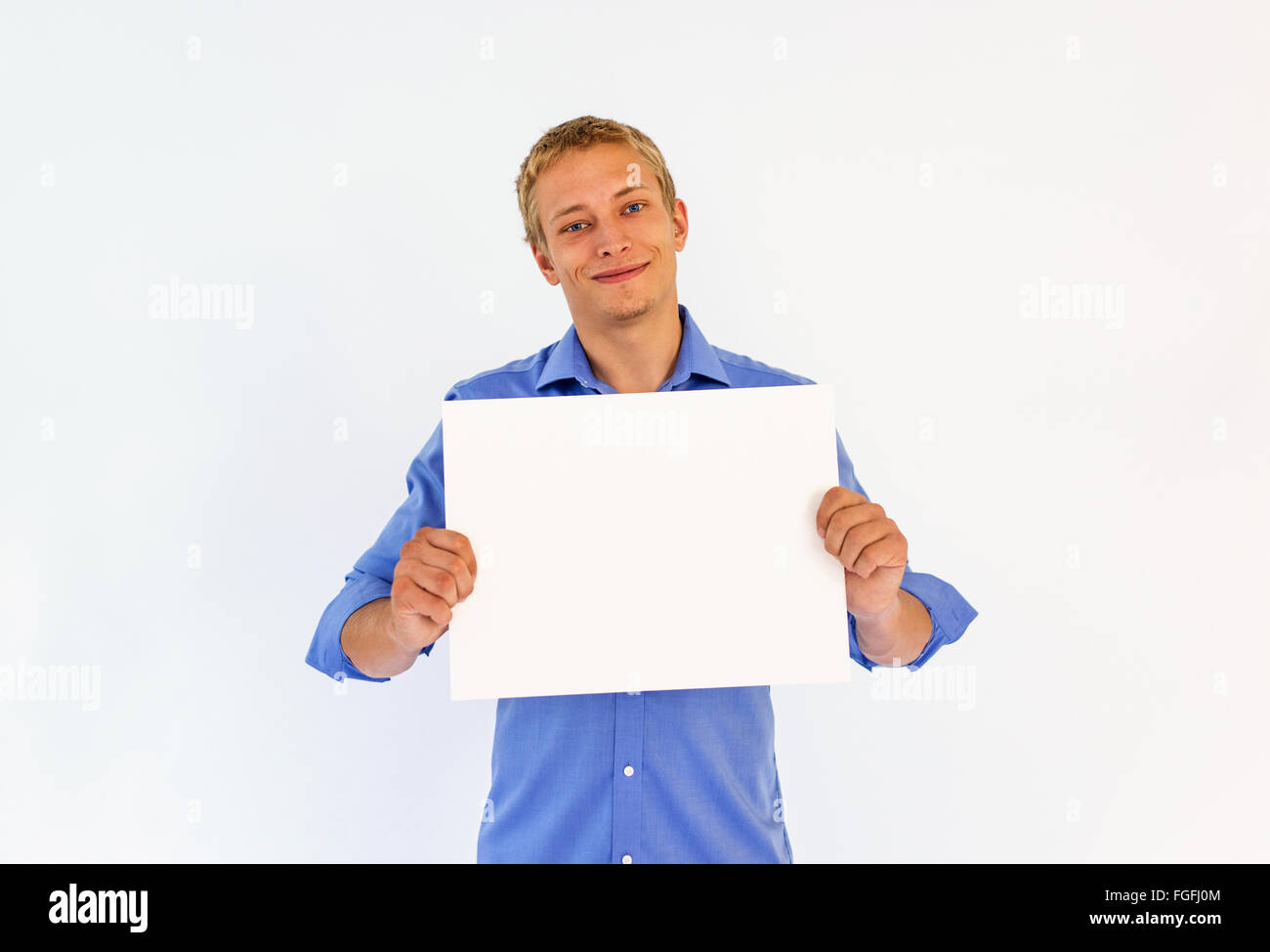 Homme portant une chemise bleu business holding a blank white morceau de carte devant sa poitrine en souriant Banque D'Images