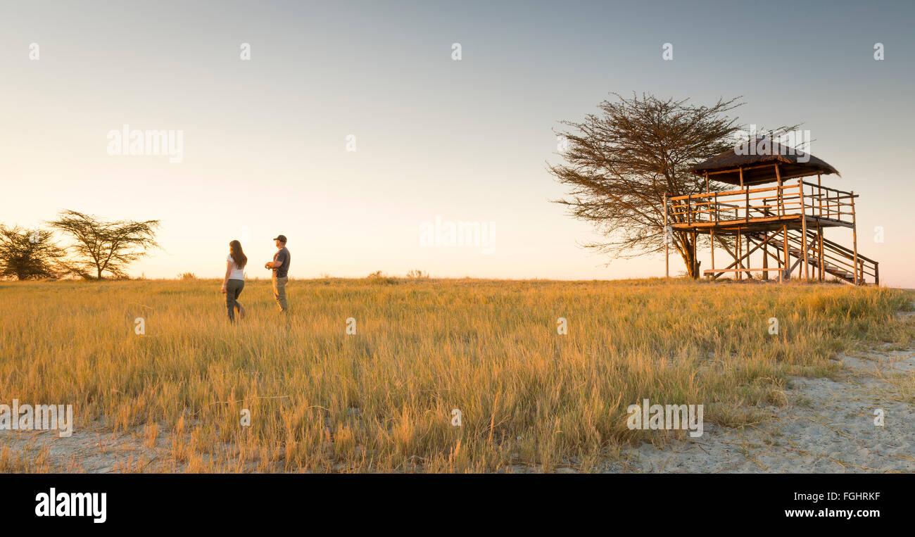 Un jeune couple stand dans l'herbe haute et regarder le coucher du soleil alors que sur safari dans le Makgadikgadi Pans, Botswana, Africa Banque D'Images