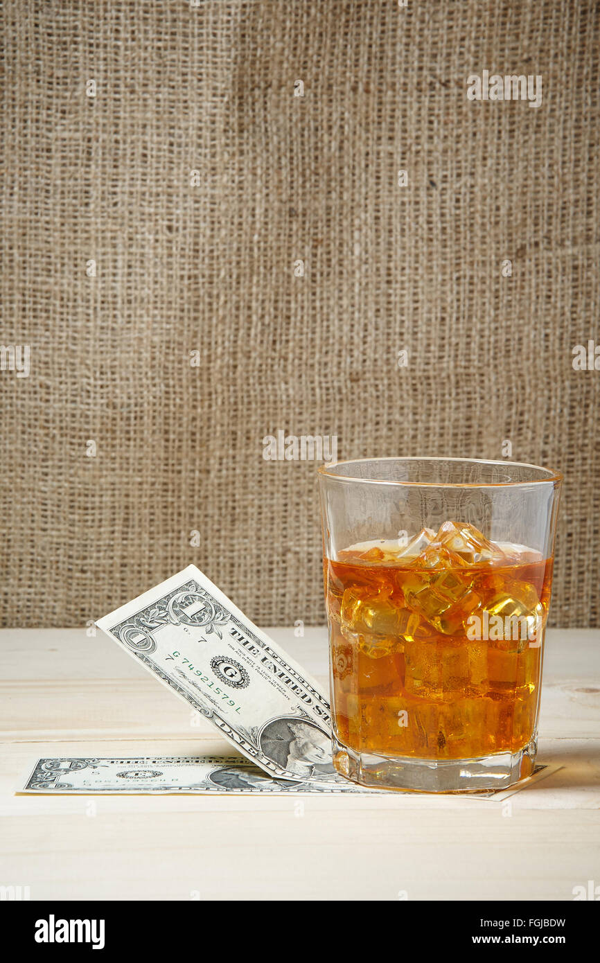 Dollars et un verre de whisky avec de la glace sur une table en bois. Place pour le texte Banque D'Images