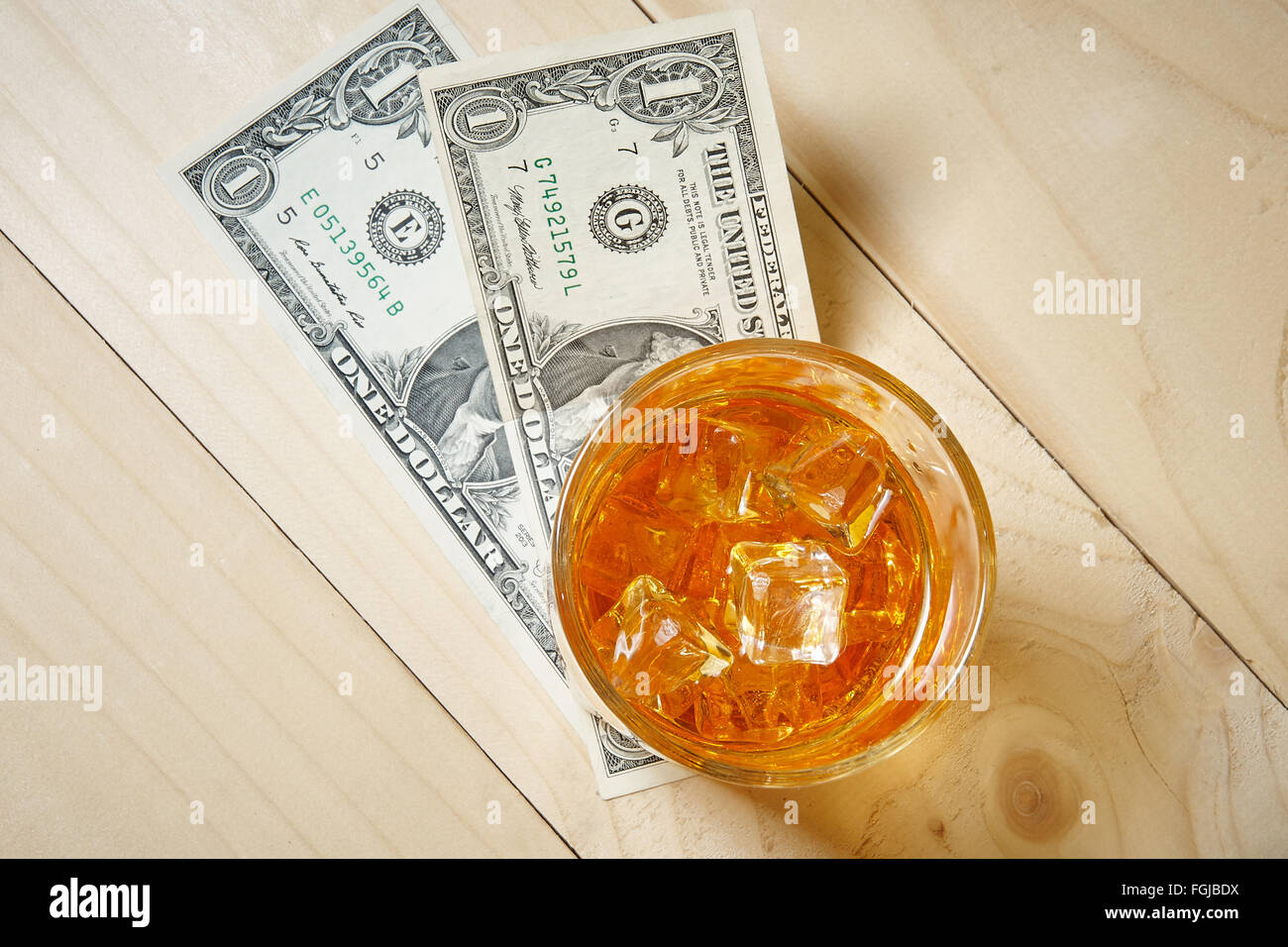 Dollars et un verre de whisky avec de la glace sur une table en bois. Vue d'en haut. Banque D'Images