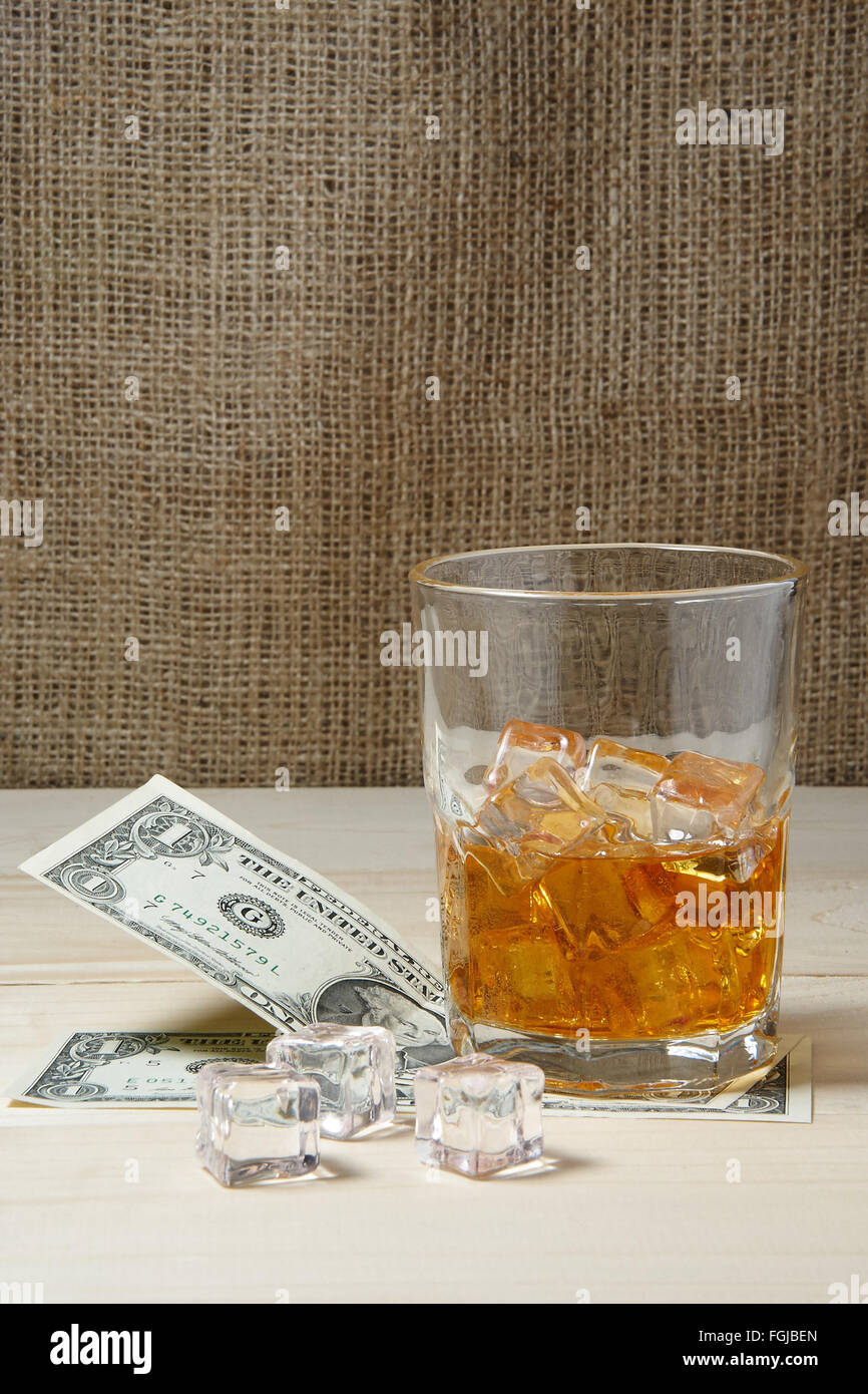 Dollars et un verre de whisky avec de la glace sur une table en bois Banque D'Images