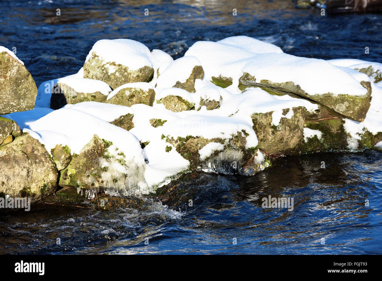 Une fine couche de neige se trouve sur quelques pierres au milieu d'une rivière. La glace a formé dans la froideur de l'eau. Banque D'Images