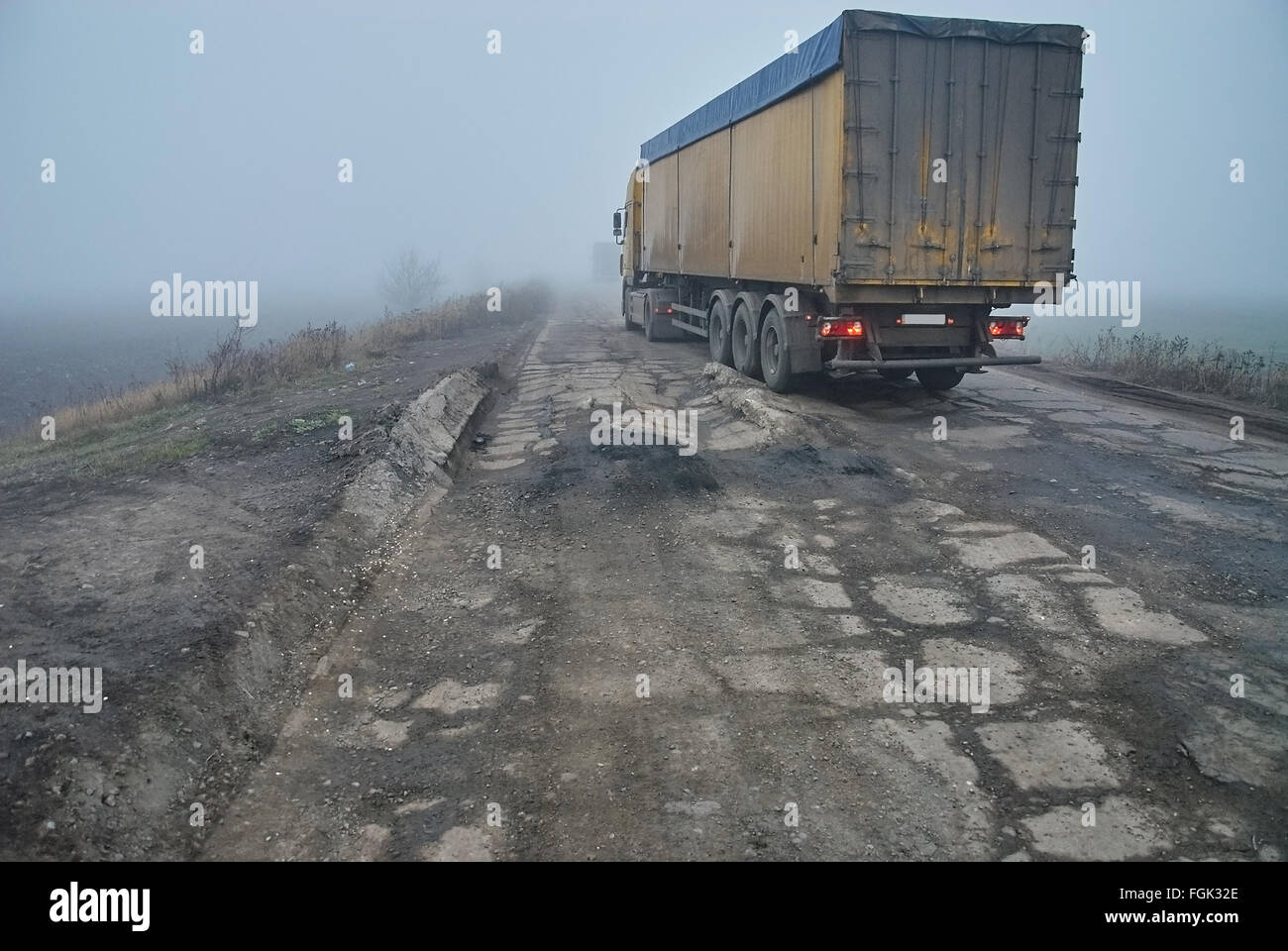 La route d'asphalte endommagé avec des nids de poule dans le brouillard. Mauvaise route. Chariot dans le brouillard. Banque D'Images