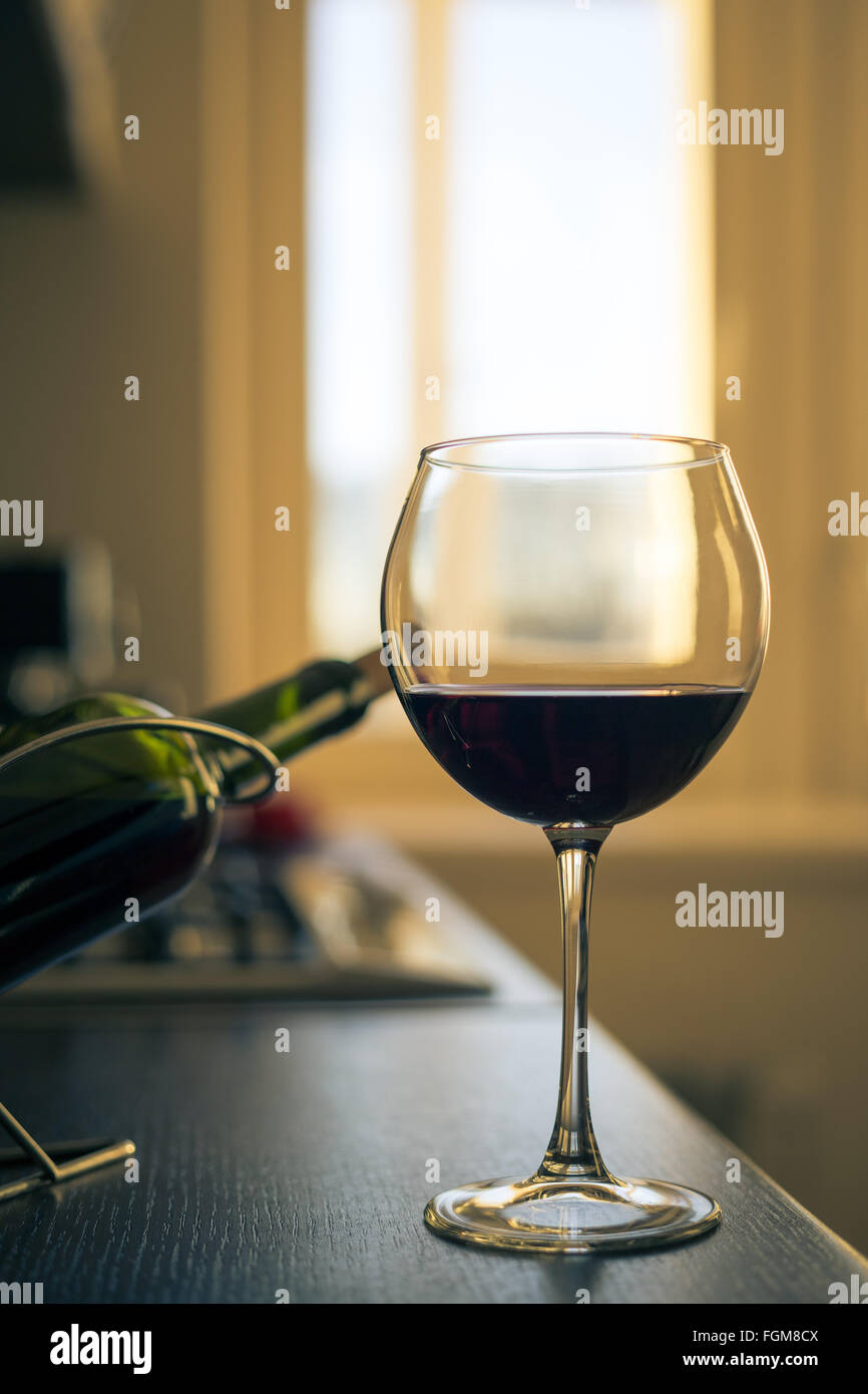 Verre de vin rouge avec une bouteille près d'une cuisine sur le plan de travail de cuisine. Banque D'Images