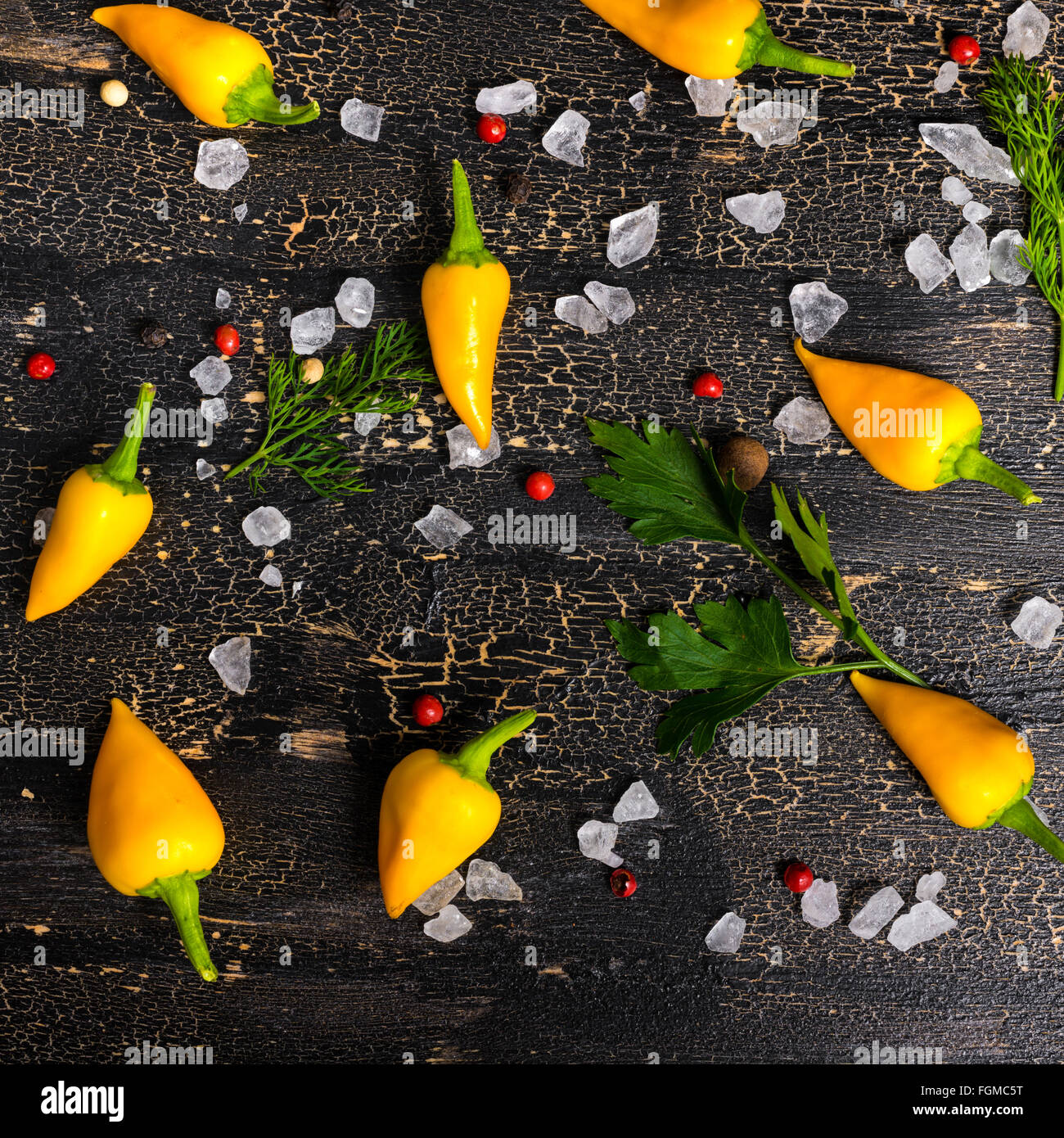 Vue de dessus de jaune Hot Chili Peppers, sel de mer, de verdure sur fond noir des fissures, Close up Banque D'Images