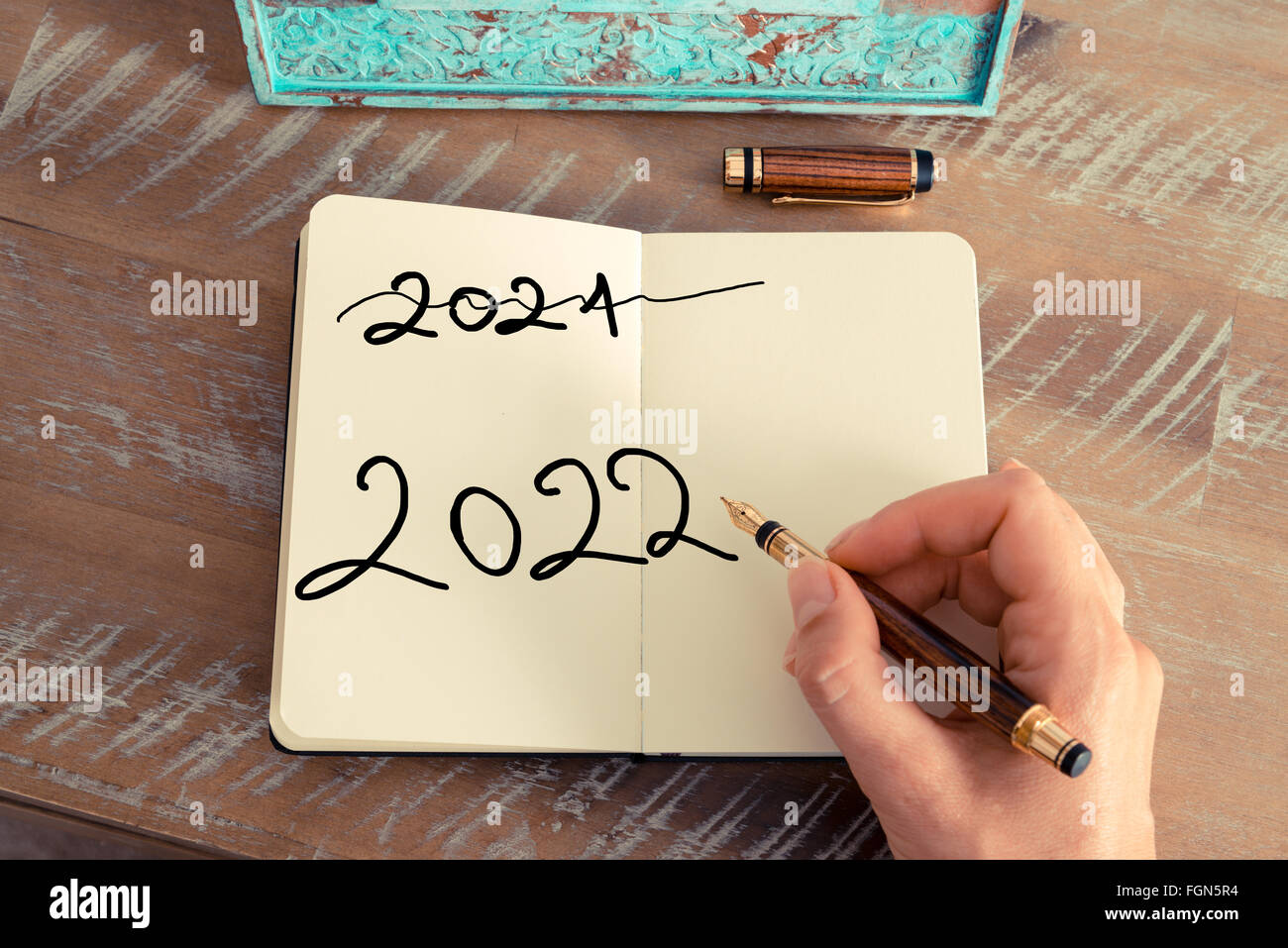 Effet rétro aux couleurs et image d'une femme d'écrire une note à la main avec un stylo sur un ordinateur portable. Concept de motivation avec texte manuscrit Bonne année 2022 et 2021 written off Banque D'Images