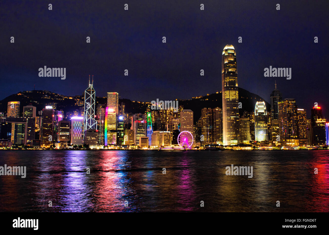 Chine Hong Kong skyline nuit harbour avec nouvelle roue de Ferris dans city skyscrapers et réflexions sur l'eau et de sommet de montagne dans la région de ba Banque D'Images