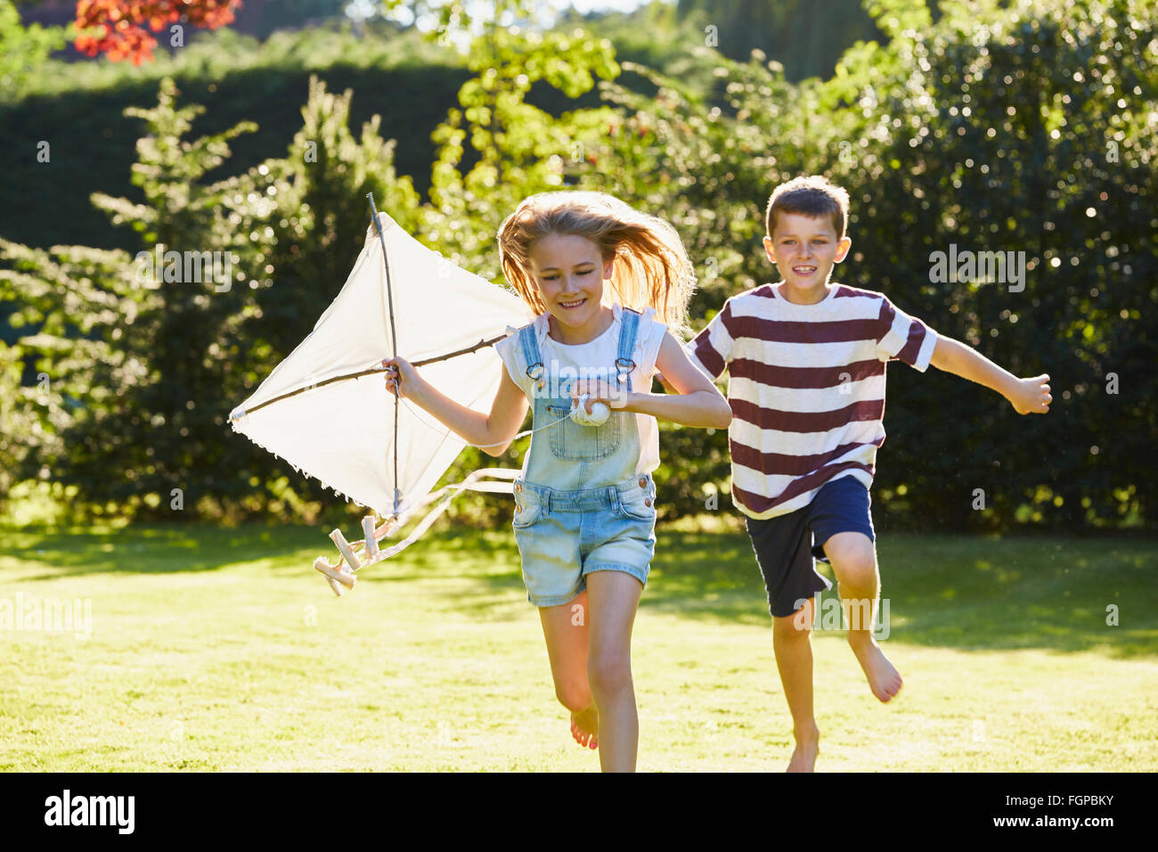Frère et sœur courir avec cerf-volant dans le jardin ensoleillé Banque D'Images Frère et sœur courir avec cerf-volant dans le jardin ensoleillé Banque D'Images