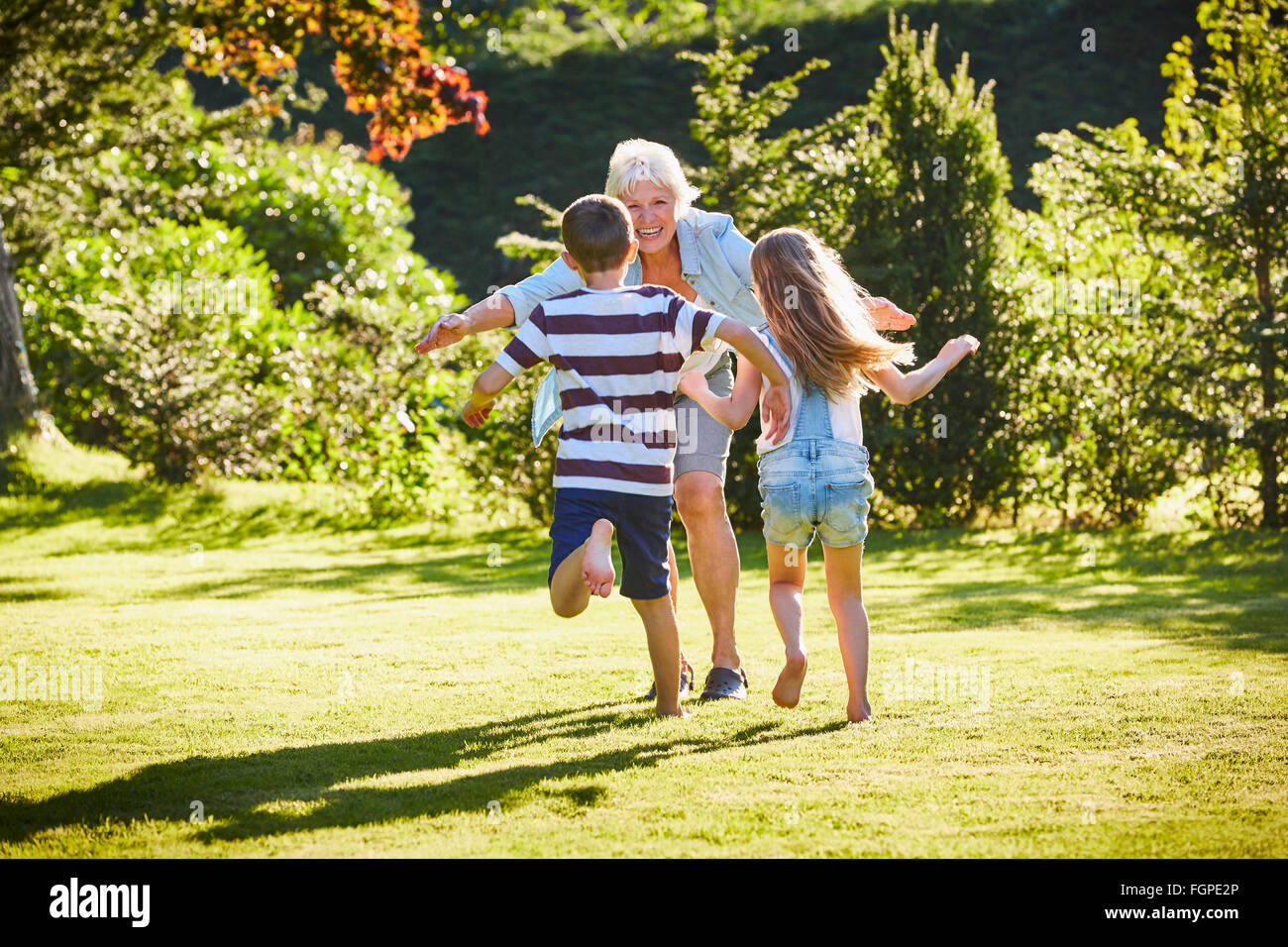 Petits-enfants courir à grand-mère dans le jardin ensoleillé Banque D'Images Petits-enfants courir à grand-mère dans le jardin ensoleillé Banque D'Images