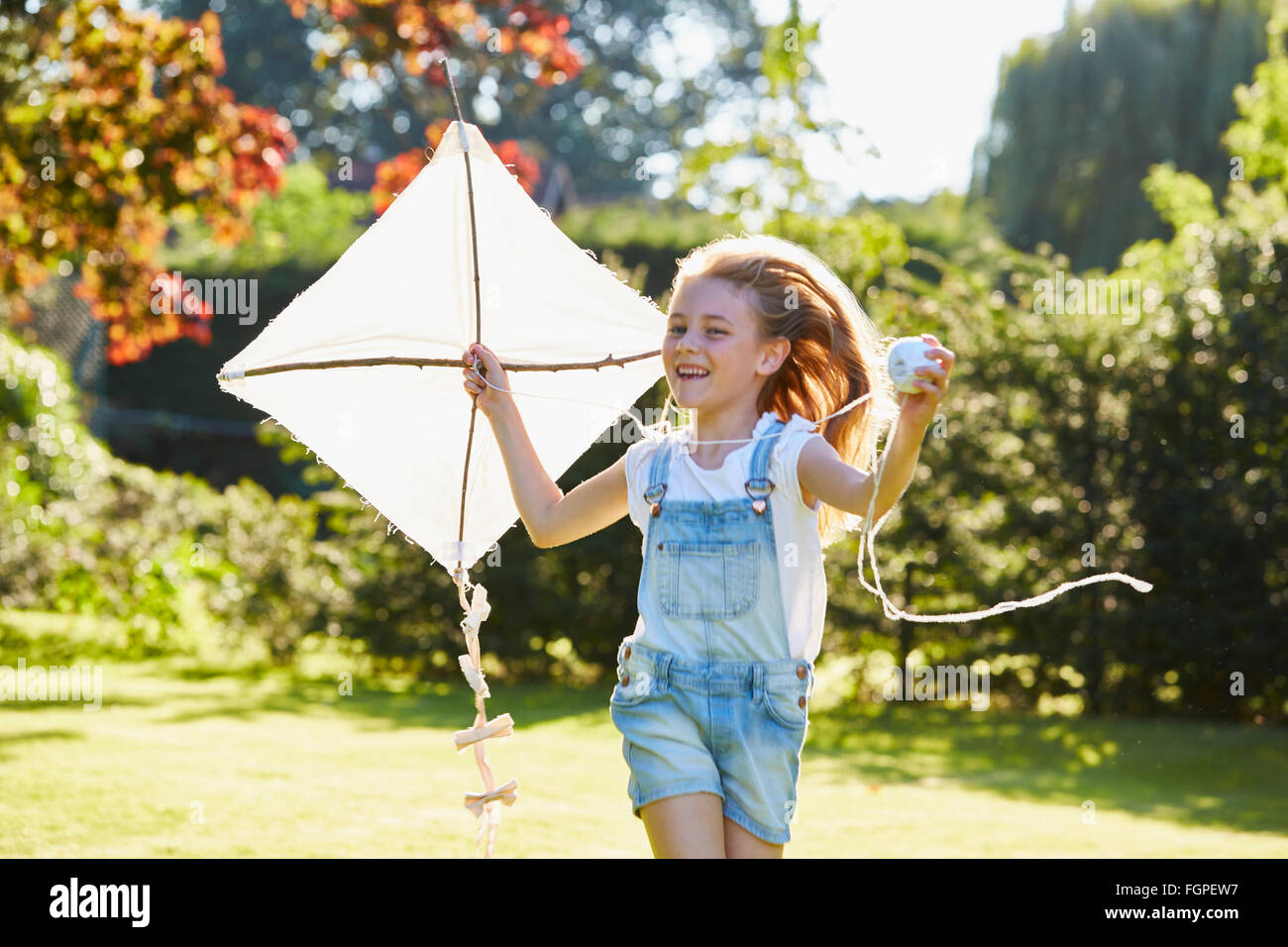 Fille courir enthousiaste avec cerf-volant dans le jardin ensoleillé Banque D'Images Fille courir enthousiaste avec cerf-volant dans le jardin ensoleillé Banque D'Images
