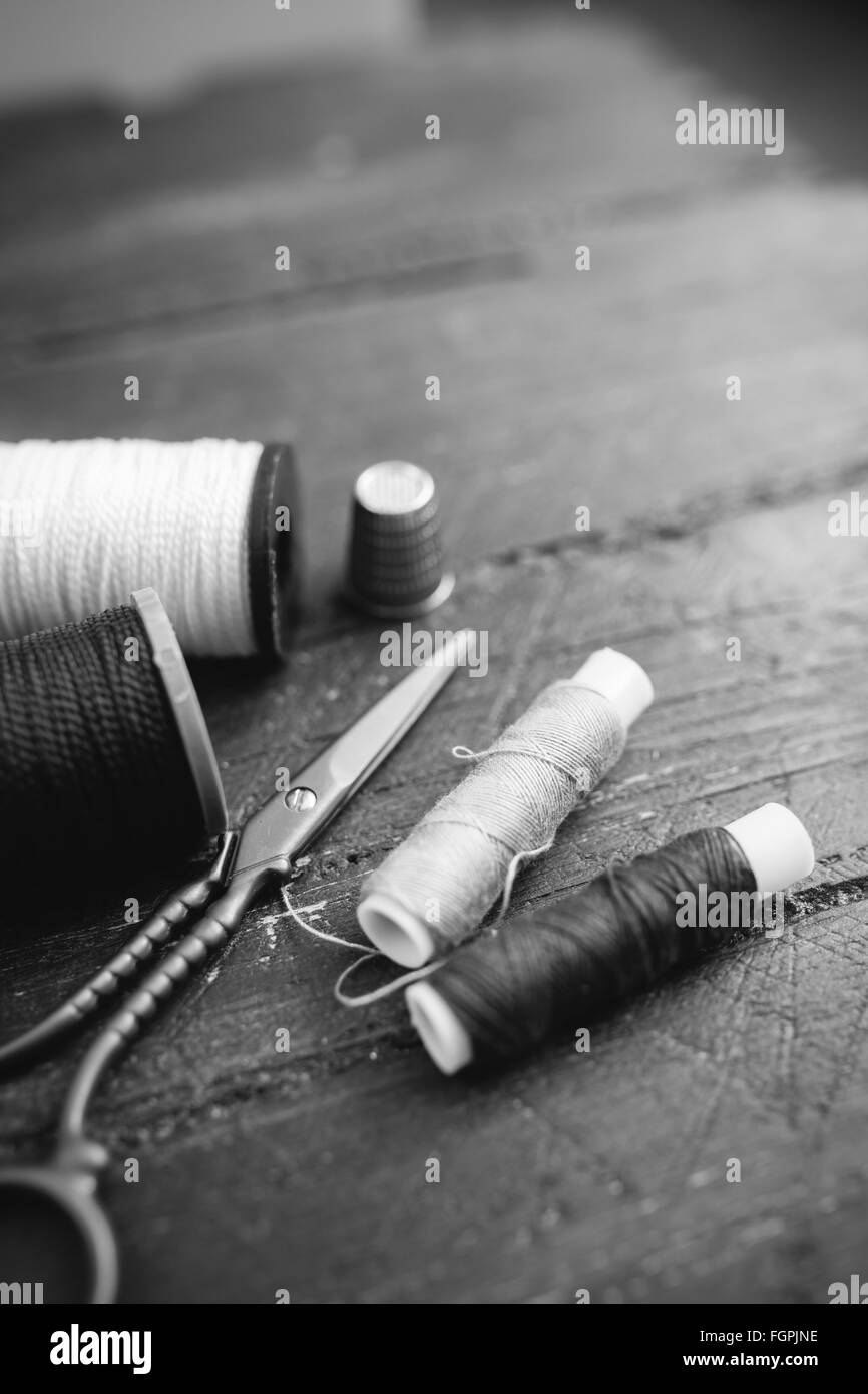 Accessoires de couture : bobines de fil, ciseaux, aiguilles, dé sur table en bois. Photo en noir et blanc. La couture et la couture concept. Banque D'Images