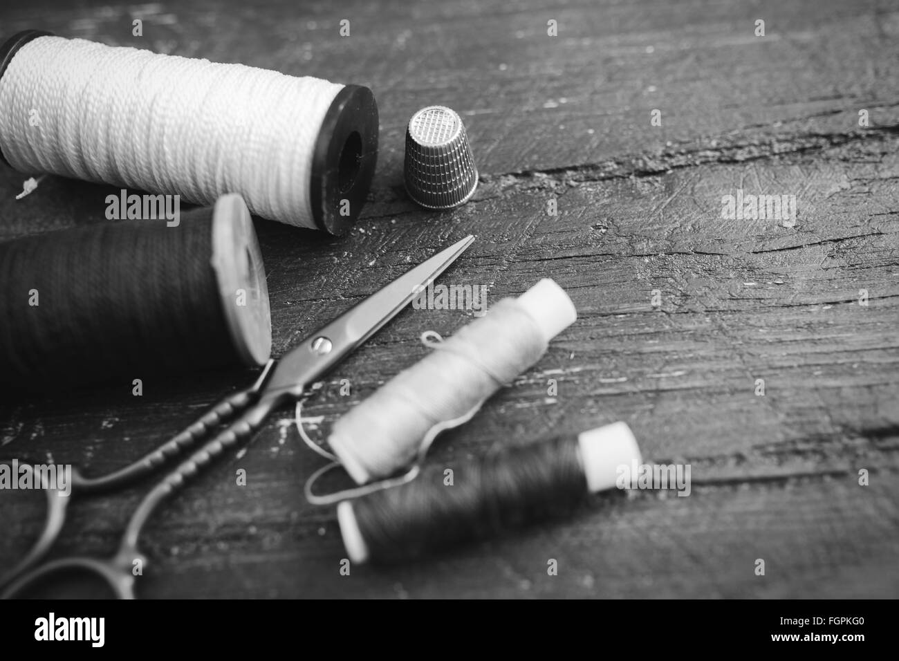 Accessoires de couture : bobines de fil, ciseaux, aiguilles, dé sur table en bois. Photo en noir et blanc. La couture et la couture concept. Banque D'Images