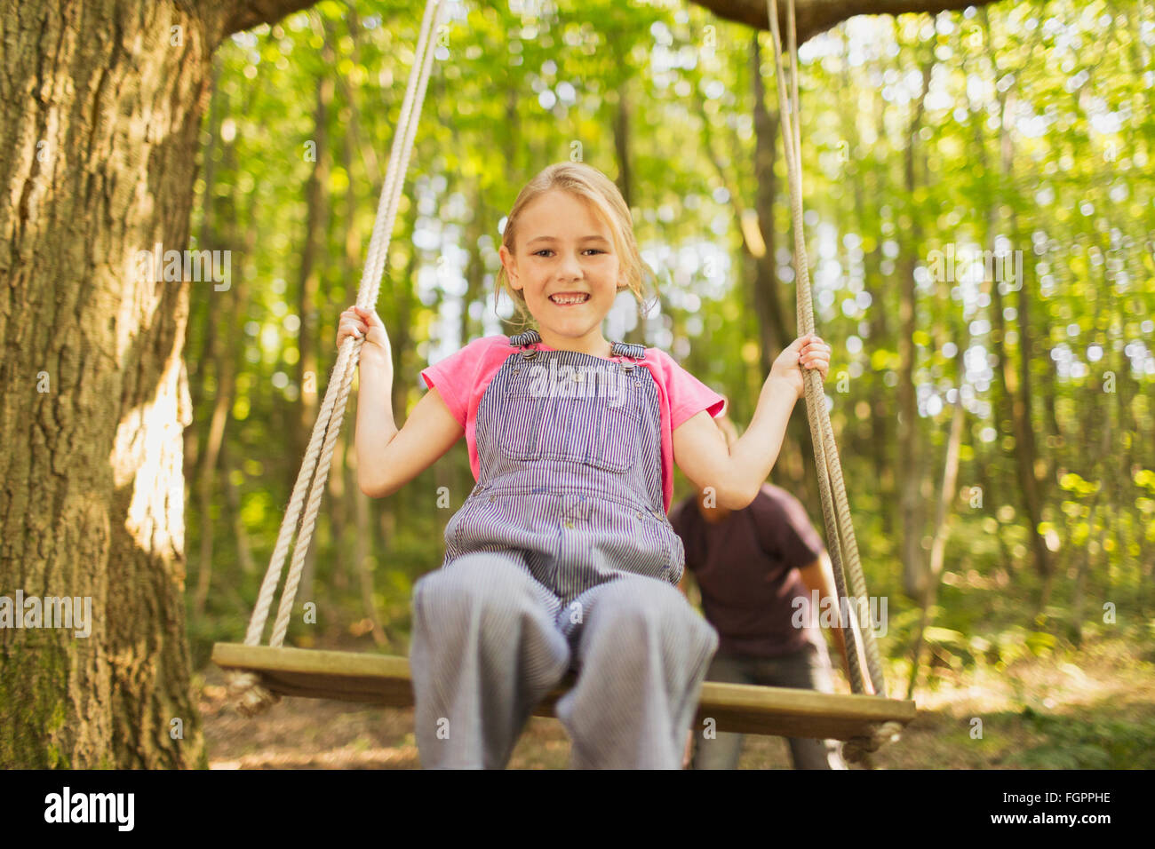 Portrait of smiling girl swinging sur rope swing in forest Banque D'Images