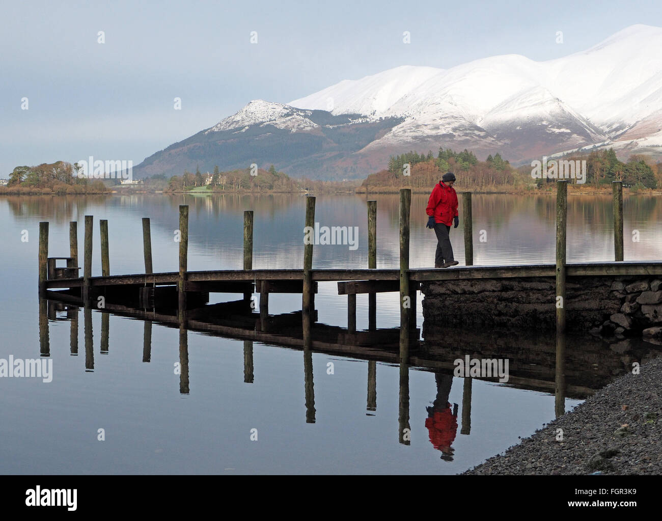 Walker avec manteau rouge sur la jetée de Derwentwater Cumbria avec collines enneigées reflète dans l'lake Banque D'Images