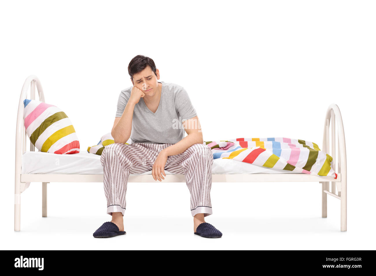 Triste jeune homme assis sur un lit et contemplant isolé sur fond blanc Banque D'Images