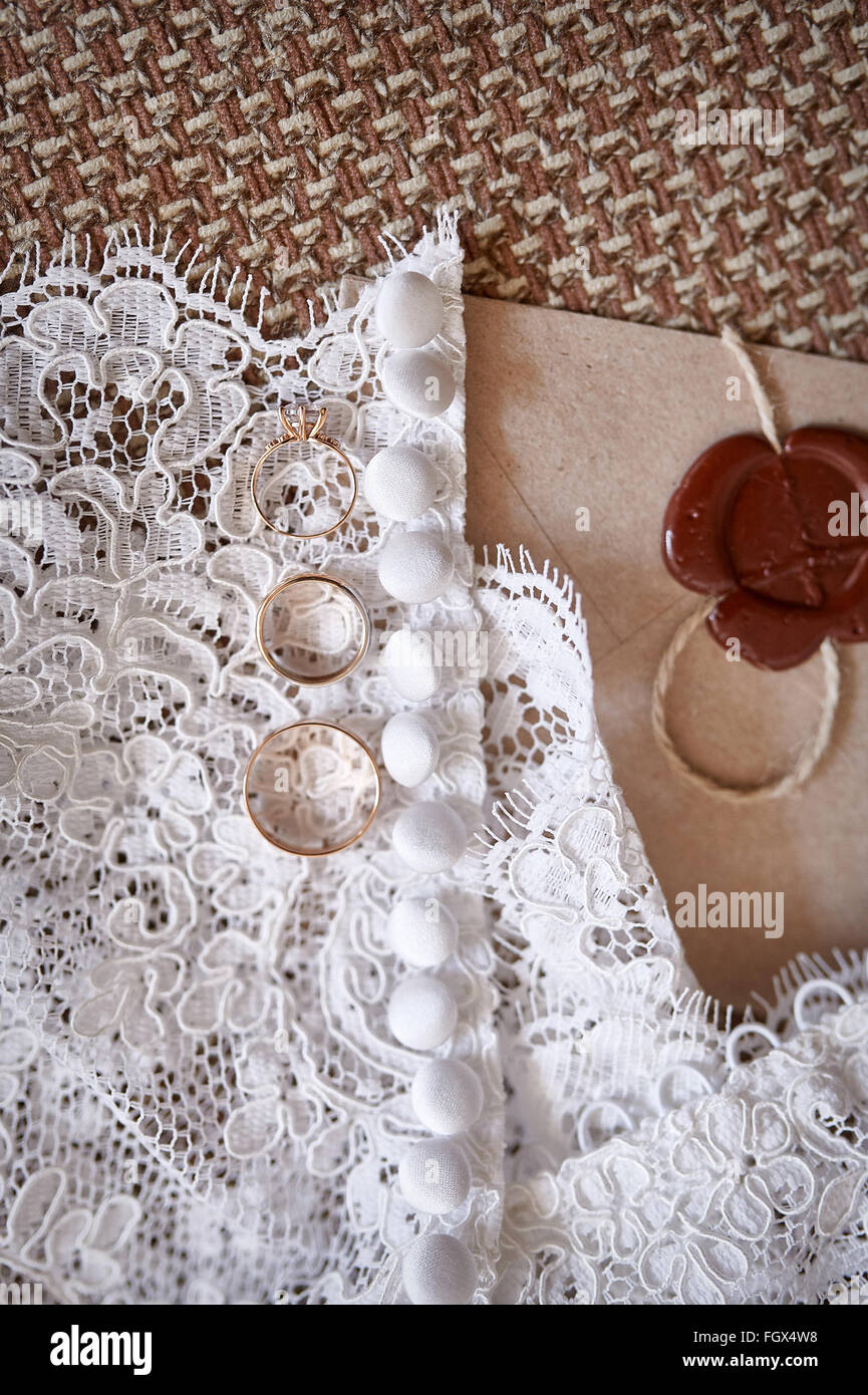 Les anneaux de mariage d'or jaune se trouvent sur une robe de la mariée Banque D'Images