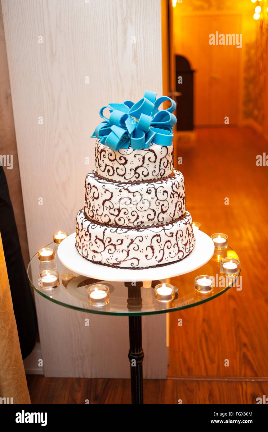 Beau blanc gâteau à trois niveaux avec un arc turquoise sur le dessus est sur la table Banque D'Images