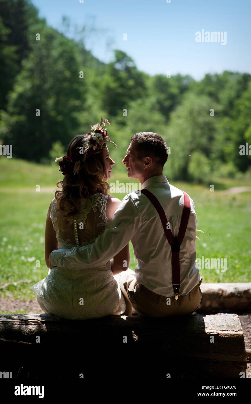 Couple de mariage mariée élégante en robe blanche et le marié élégant assis sur un banc dans le parc Banque D'Images