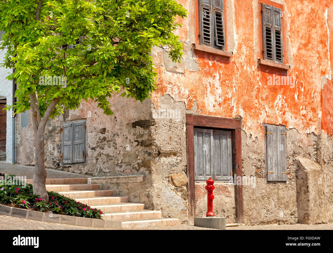 Old red corner house historique avec de murs et fenêtres, de l'obturateur sur la rue pavée, avec de l'eau rouge d'incendie et un arbre en face Banque D'Images