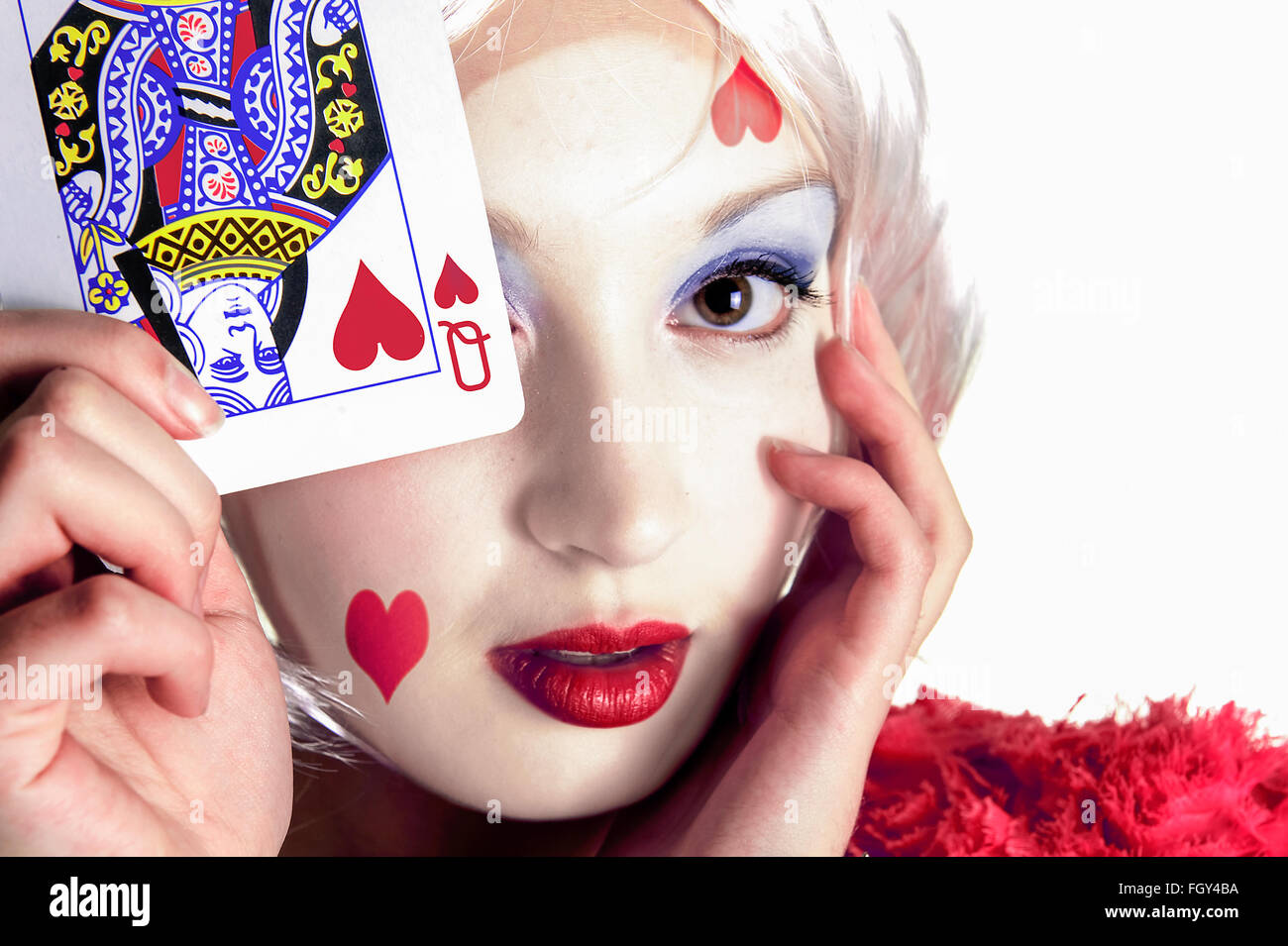 Jeune femme tenant une carte à jouer près de son visage avec la reine de cœur sur la carte et le visage Banque D'Images