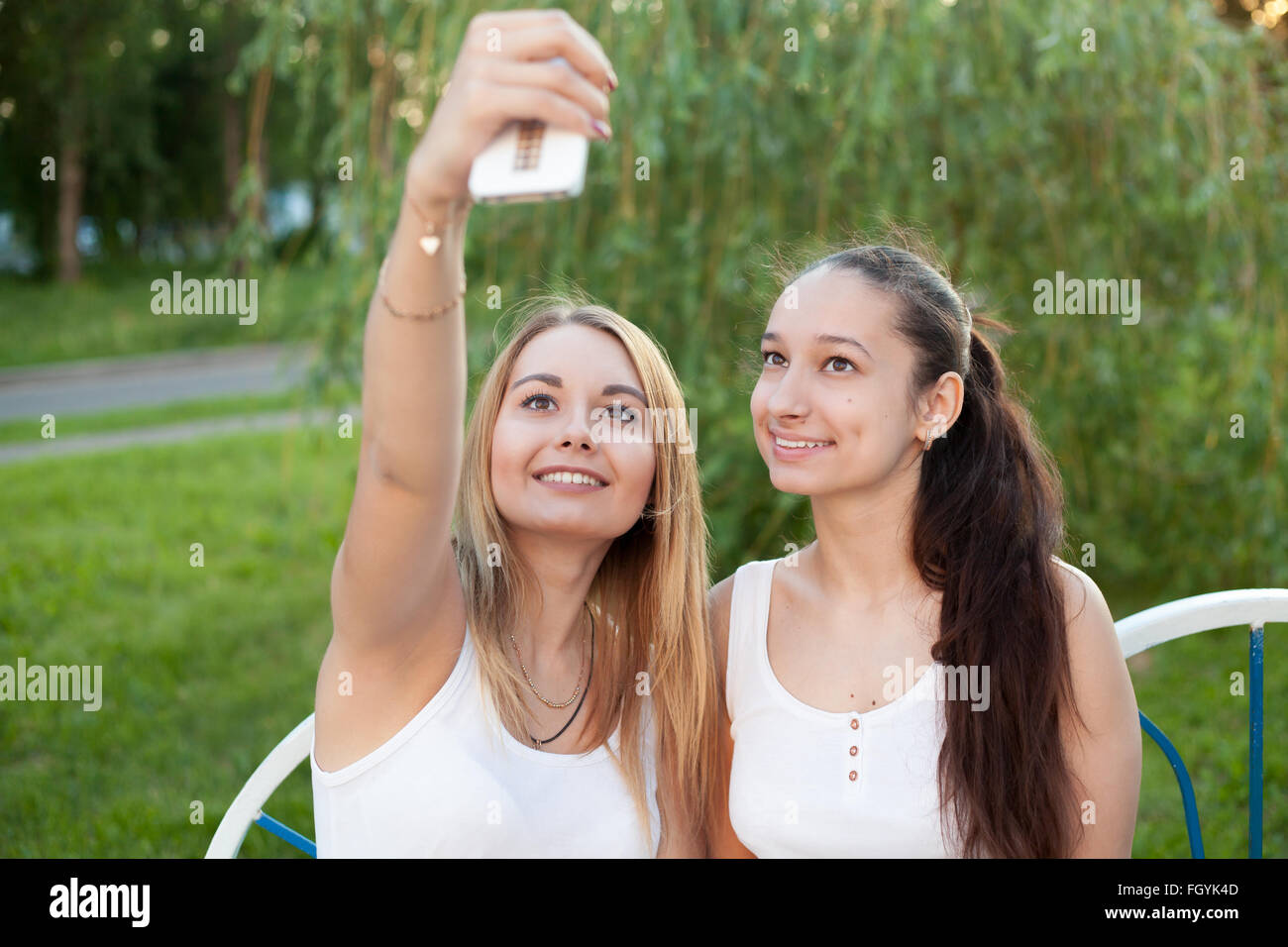 Deux belles jeunes femmes happy smiling friends portant des vêtements décontractés assis sur banc de parc sur la prise de jour d'selfies Banque D'Images