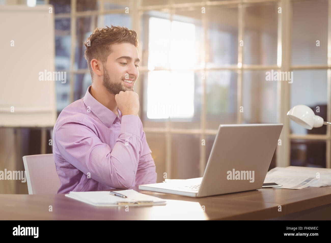 Businessman with hand on chin travaillant avec un ordinateur portable Banque D'Images