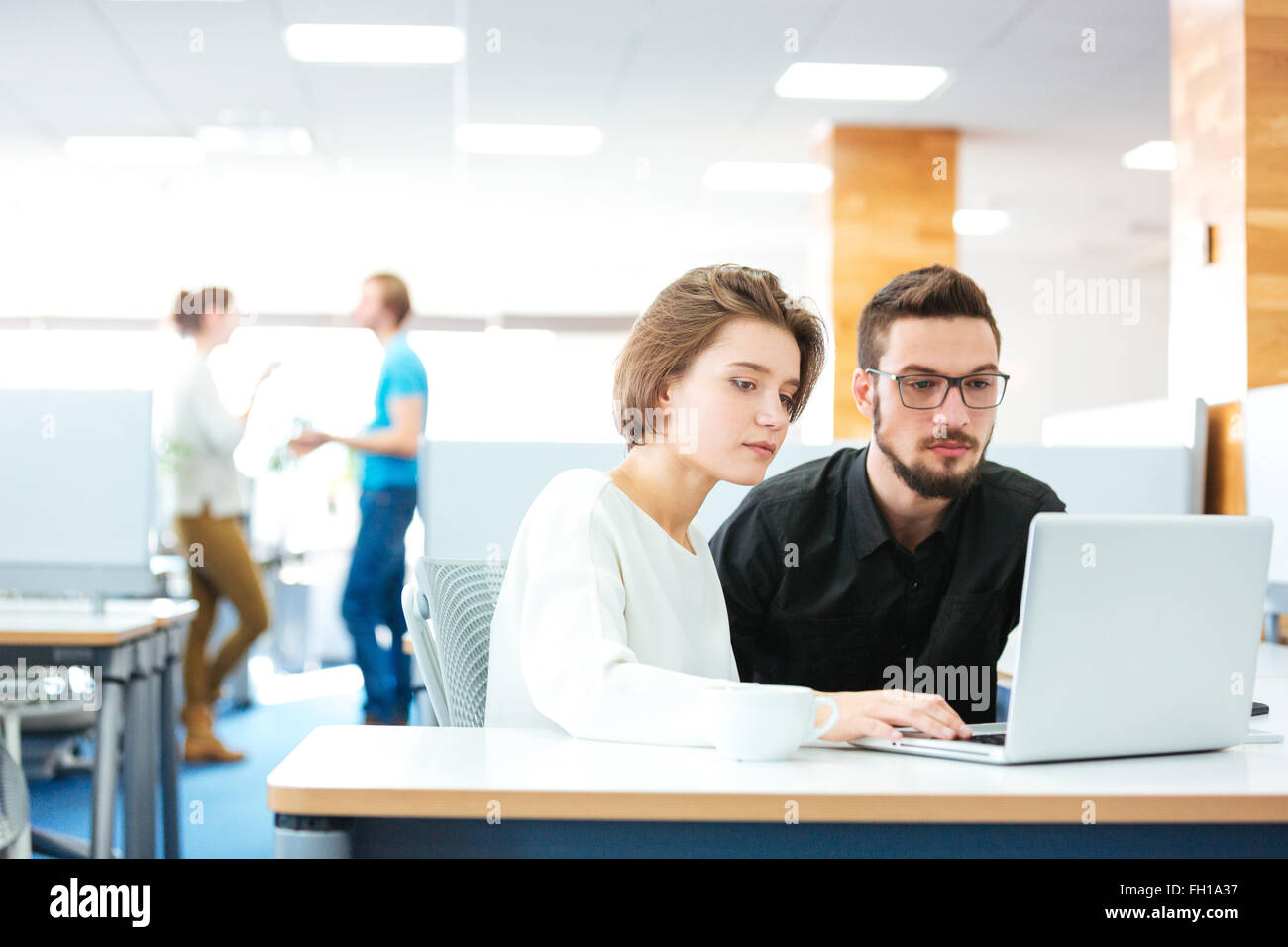 L'accent grave jeune homme et femme assise et travailler avec laptop in office Banque D'Images