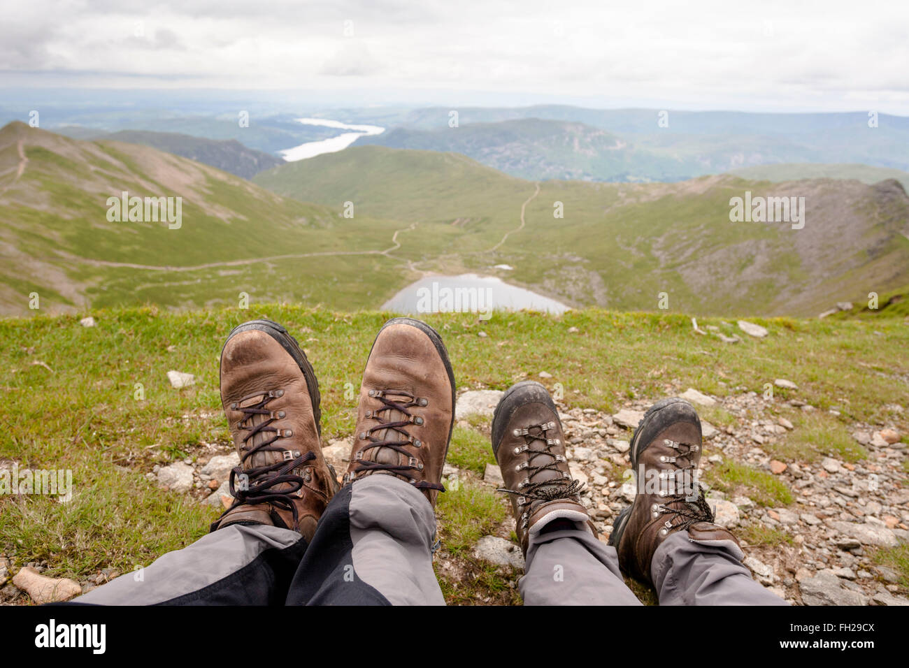 À la recherche de rouge Tarn au-delà de bottes de randonnée de deux randonneurs reposant sur Helvellyn, Lake District, Cumbria, England, United Kingdo Banque D'Images