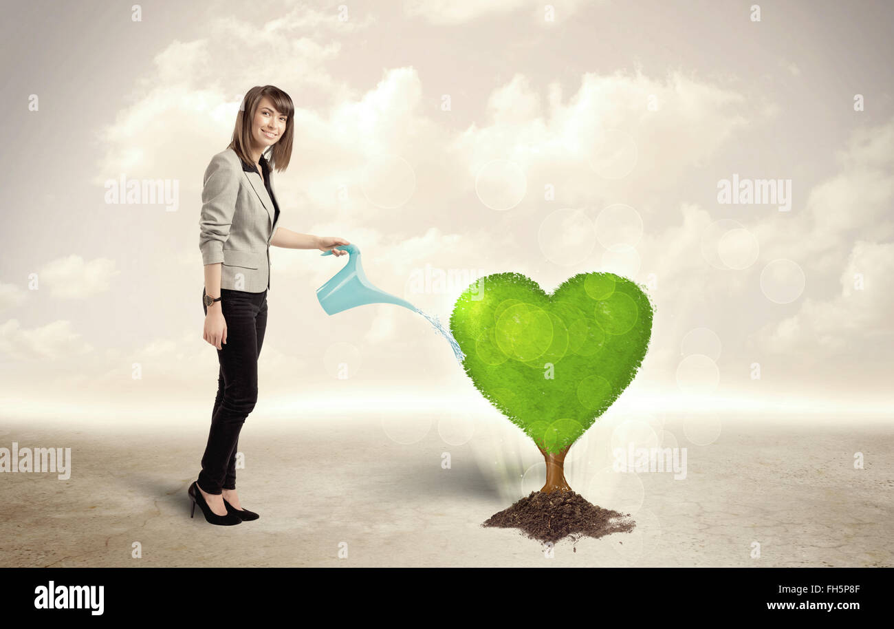 Femme d'affaires d'arroser l'arbre vert en forme de coeur Banque D'Images