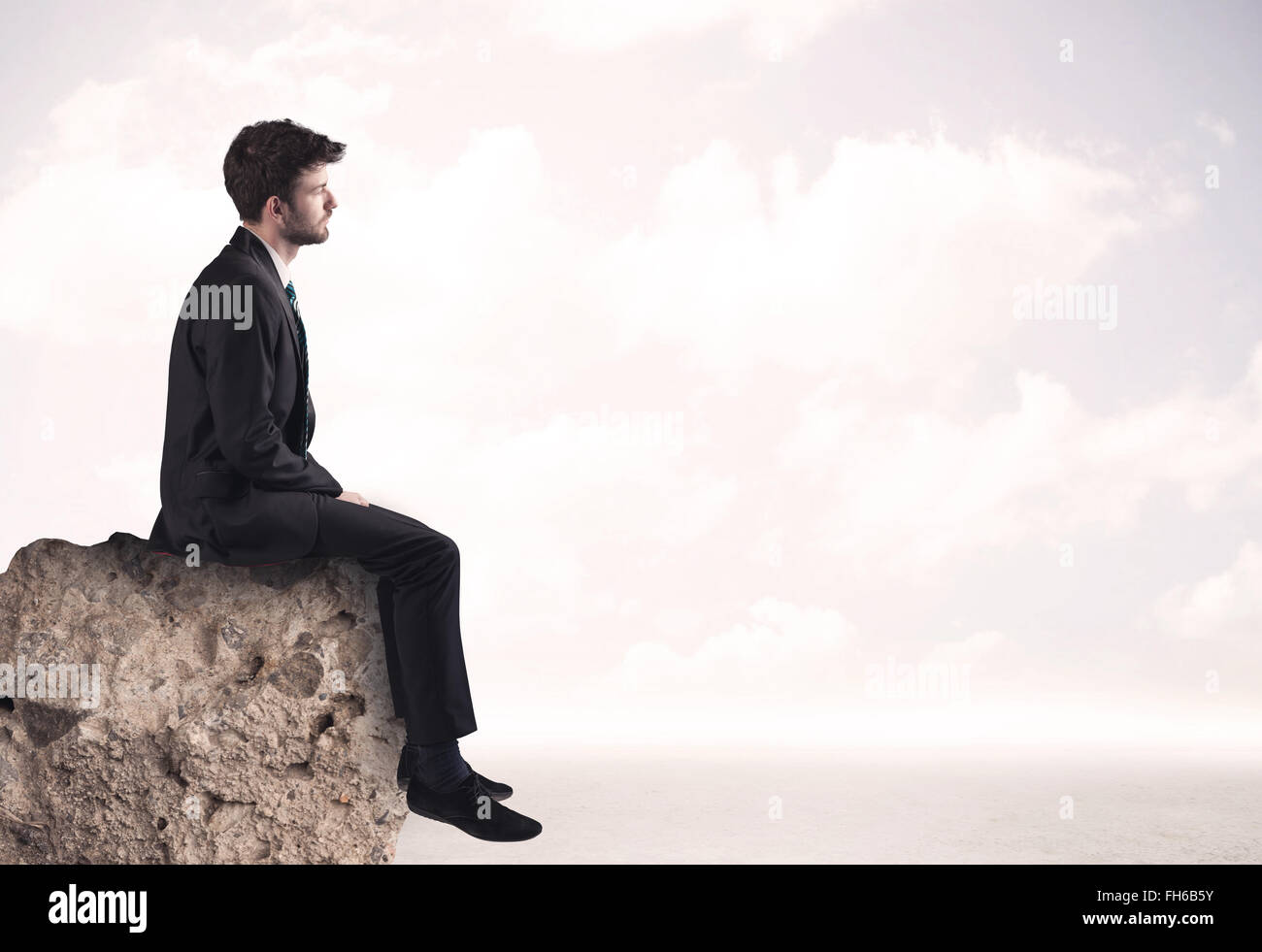 Business man sitting on stone edge Banque D'Images