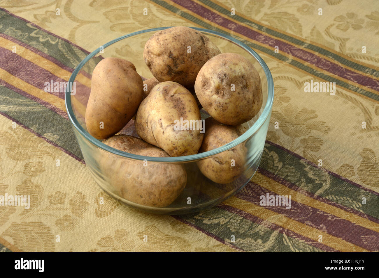 Matières premières non cuit les pommes de terre roussâtres dans bol en verre sur la table Banque D'Images