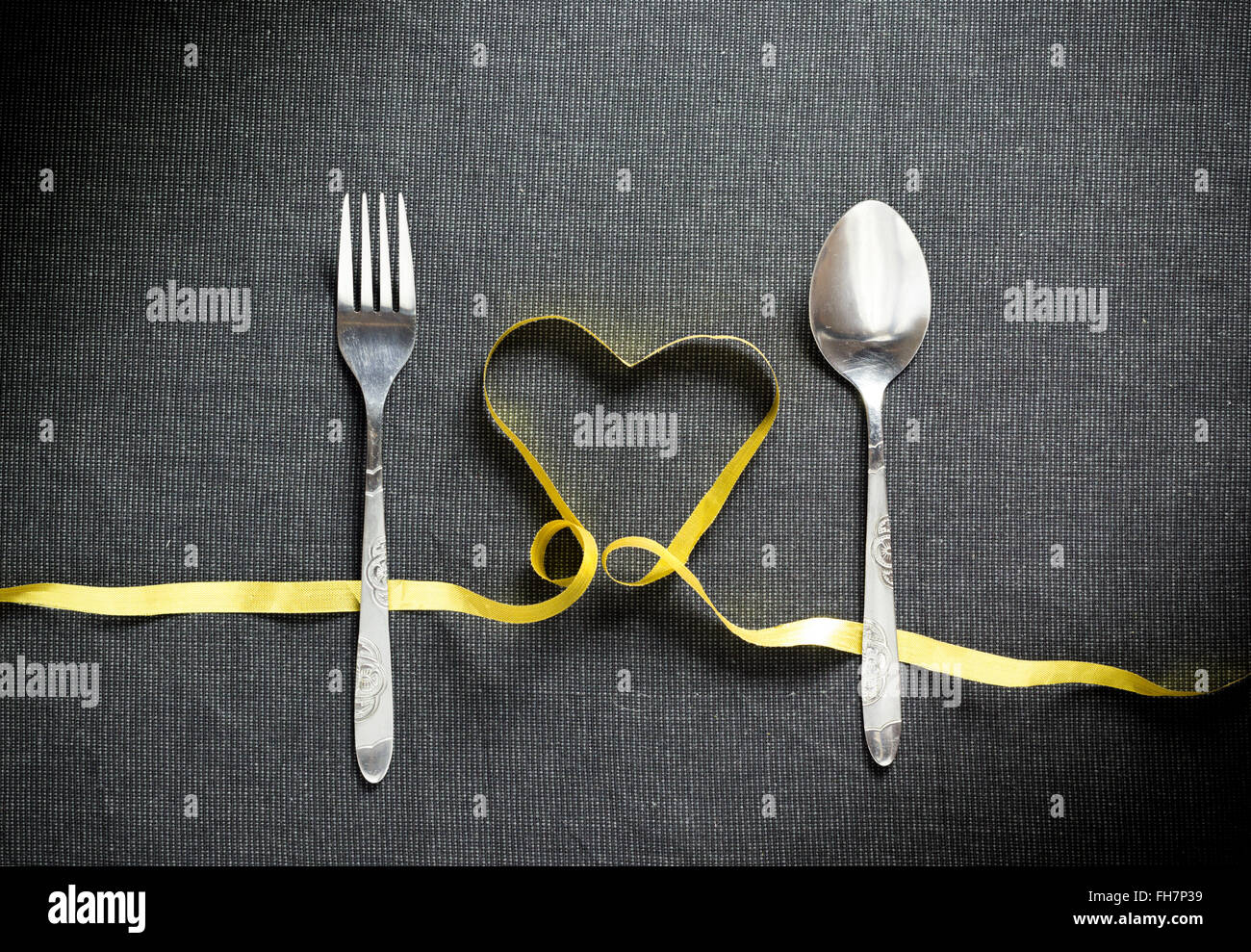 Fourchette et cuillère en forme de coeur fait de ruban jaune sur fond texturé noir Banque D'Images