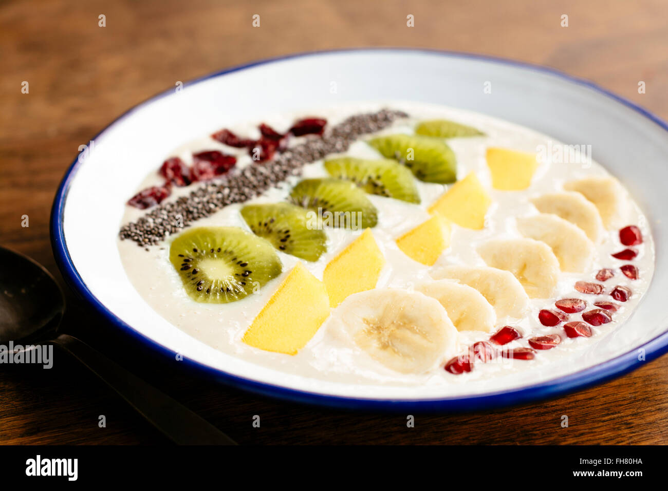 Smoothie banane bol avec kiwi, mangue, banane, chia seeds, canneberges séchées et pommegranate arils comme garniture. Banque D'Images