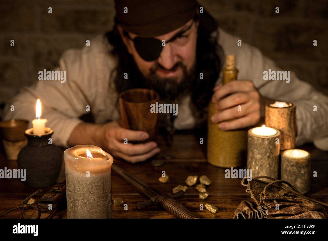Grognon pirate avec une bouteille de rhum assis sur une table médiévale avec beaucoup de bougies Banque D'Images