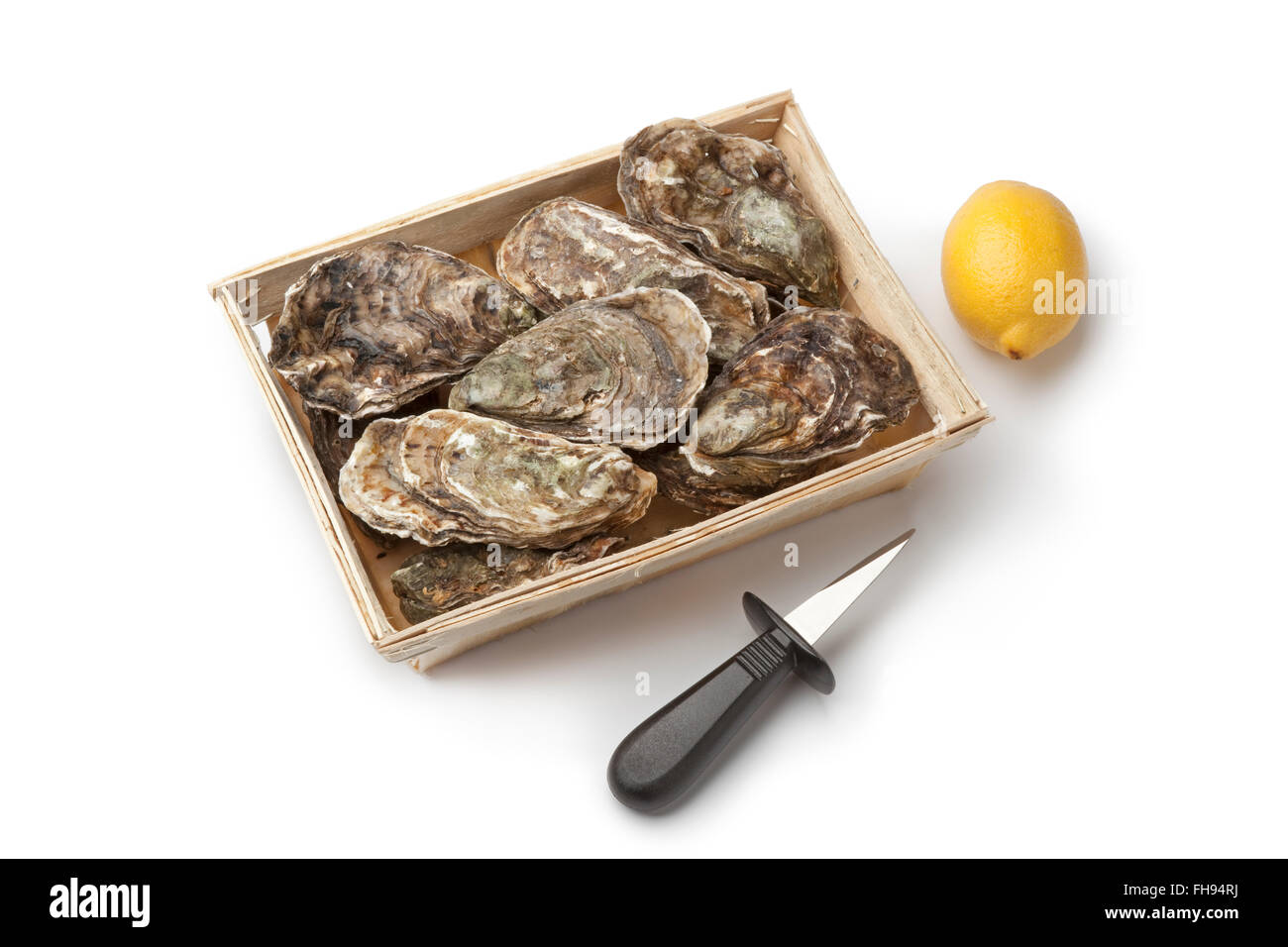 Des huîtres crues dans une boîte avec un couteau à huîtres et citron sur fond blanc Banque D'Images
