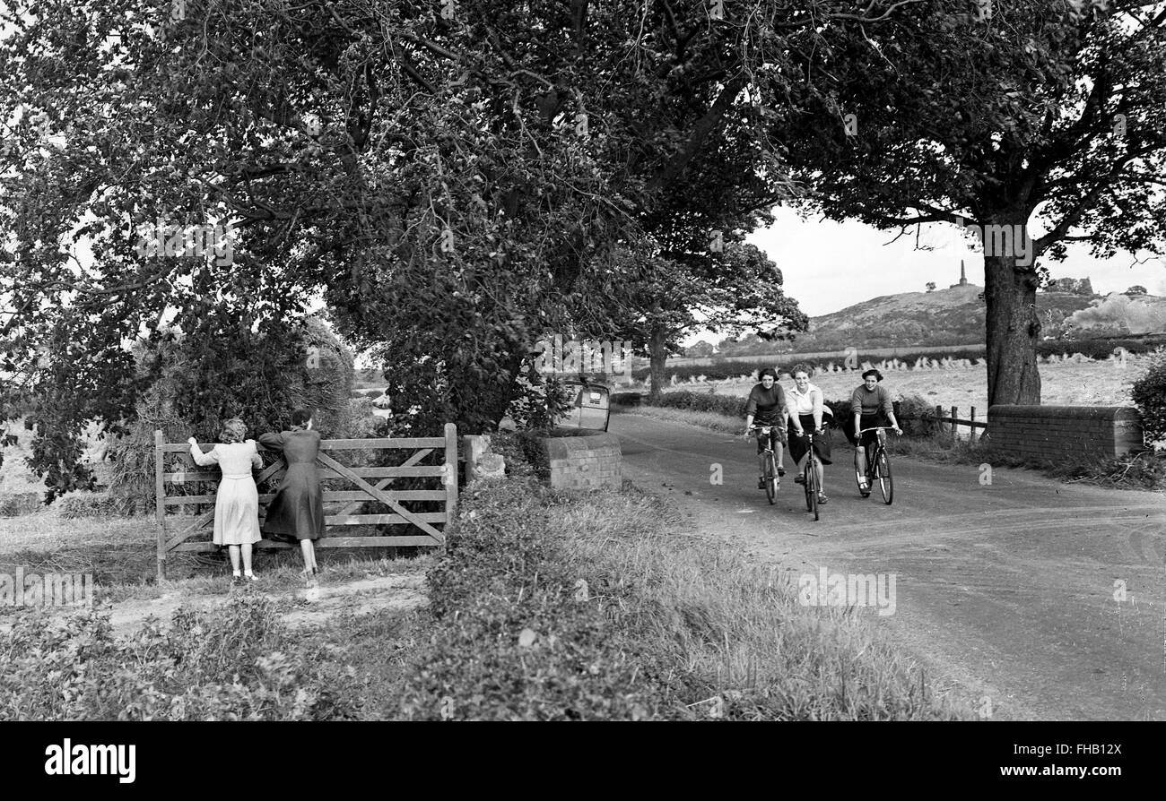 Les filles riding bike vers le bas une route de campagne en été Shropshire England Uk 1950 Banque D'Images