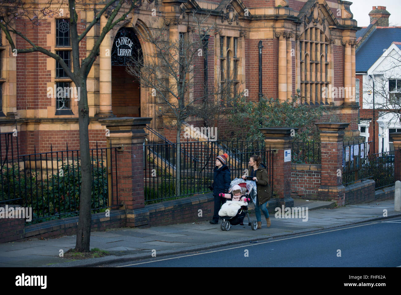 Une mère conduit ses enfants au-delà de la façade extérieure de la Bibliothèque Carnegie à Herne Hill. Face à la fermeture de sa bibliothèque locale, plan de Lambeth pour fermer l'installation utilisée par la communauté dans le cadre d'austérité, disant qu'ils vont convertir l'immeuble en un sport et entreprises privées embourgeoisés - plutôt qu'un bien-aimé la lecture et ressource d'apprentissage. 12 600 € a été donné par l'American philanthrope Andrew Carnegie pour aider à construire la bibliothèque qui a ouvert ses portes en 1906. Banque D'Images