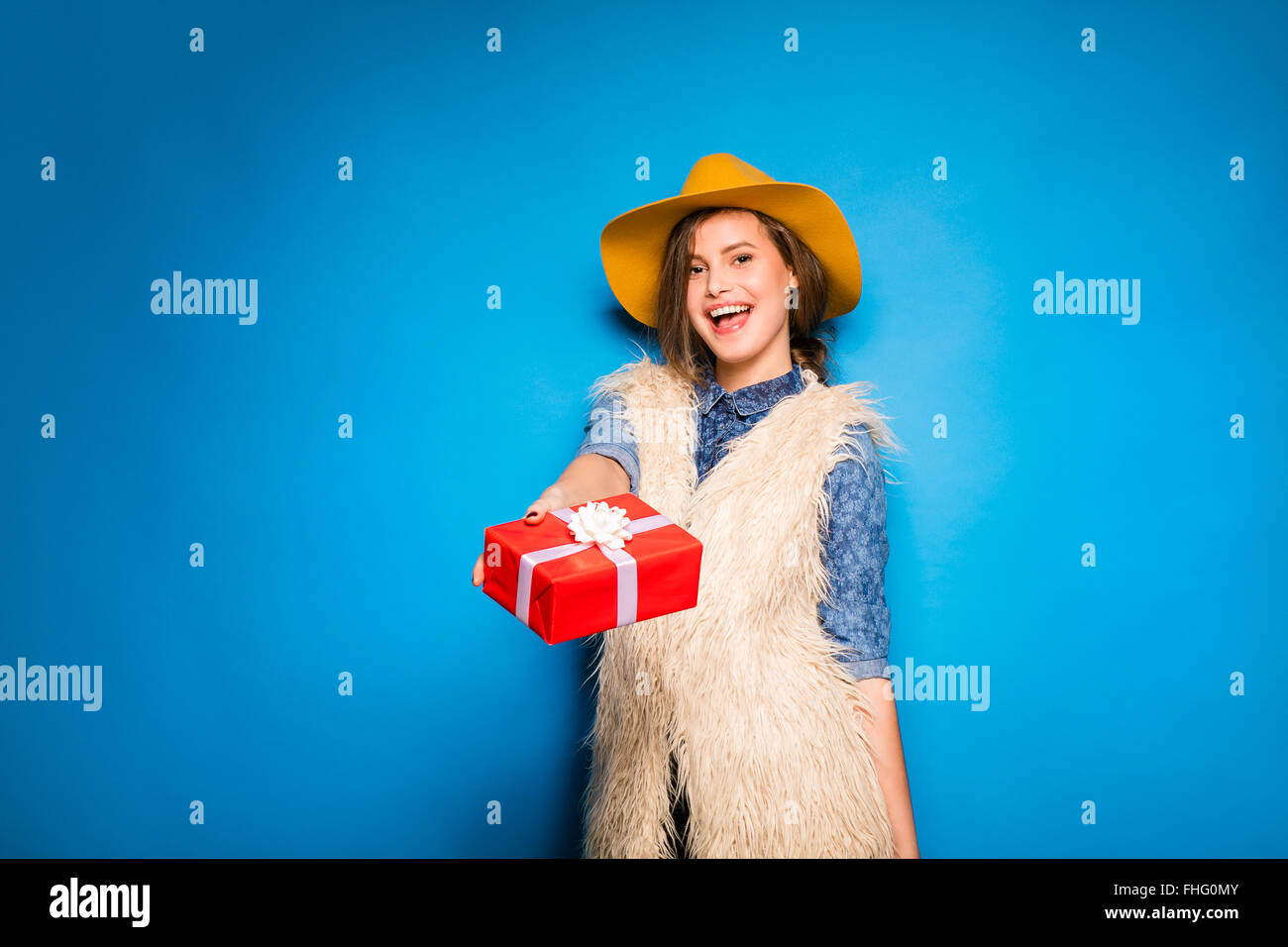 Jeune femme moderne offrant un cadeau, rouge sur fond bleu Banque D'Images