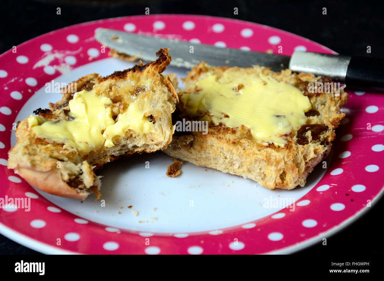 Un hot cross bun, réduit de moitié, grillé et de beurre. Une des moitiés a eu une morsure. Banque D'Images