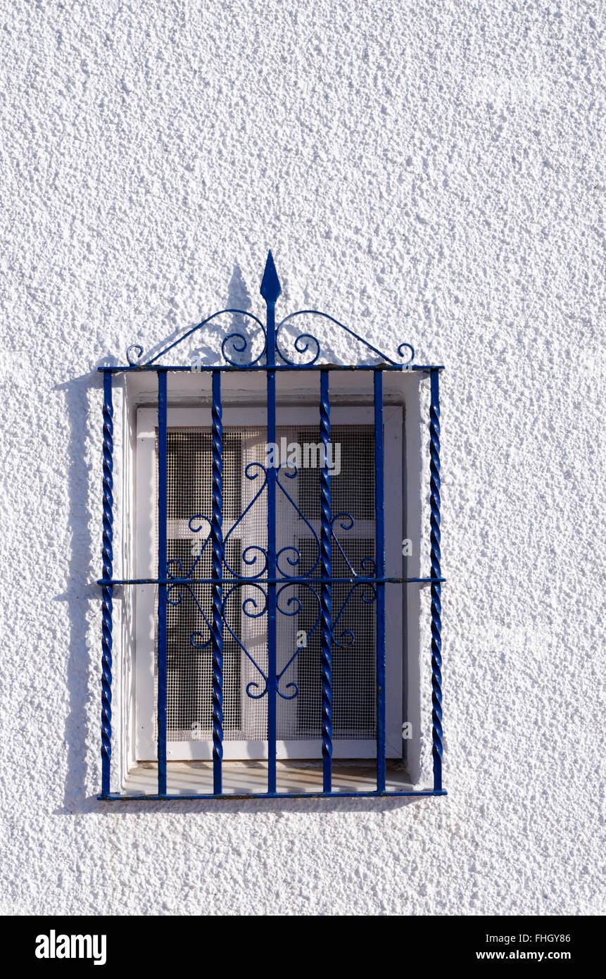 Petite fenêtre avec une grille décorative bleu sur un mur blanc d'une maison espagnole Banque D'Images