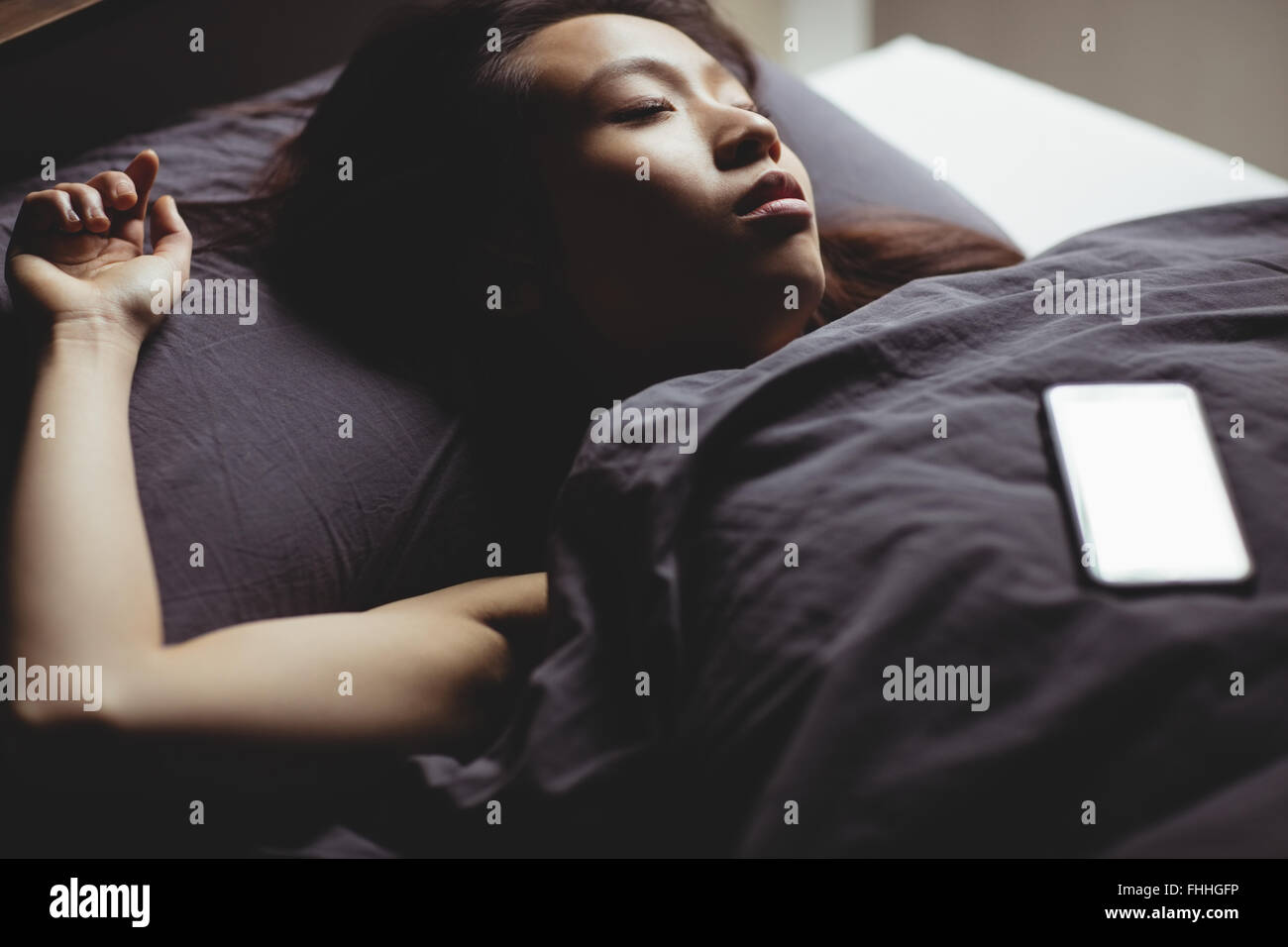 Brunette dormir sur le lit avec smartphone Banque D'Images