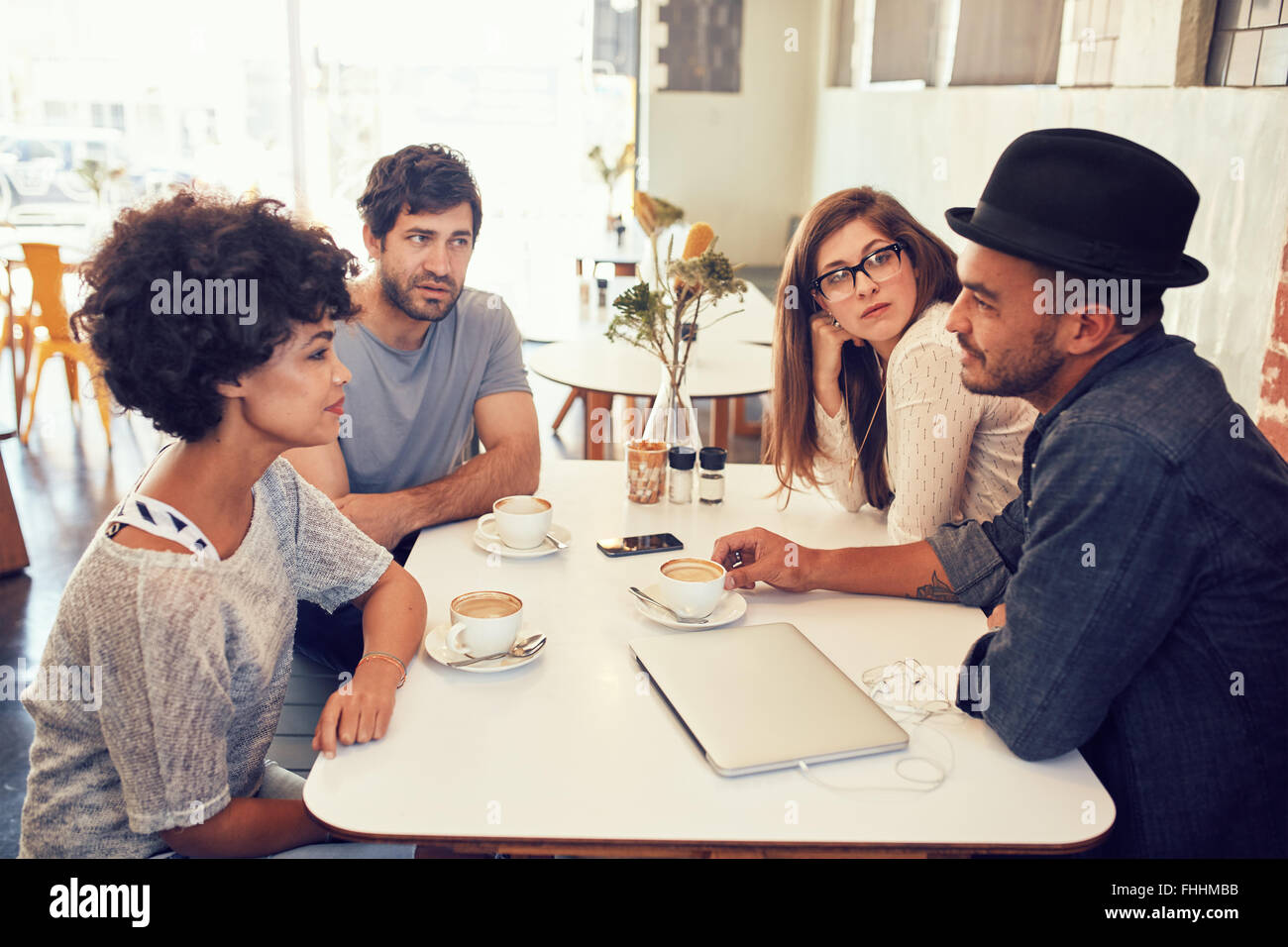 Portrait de jeunes hommes et femmes assis à une table de café et de ...