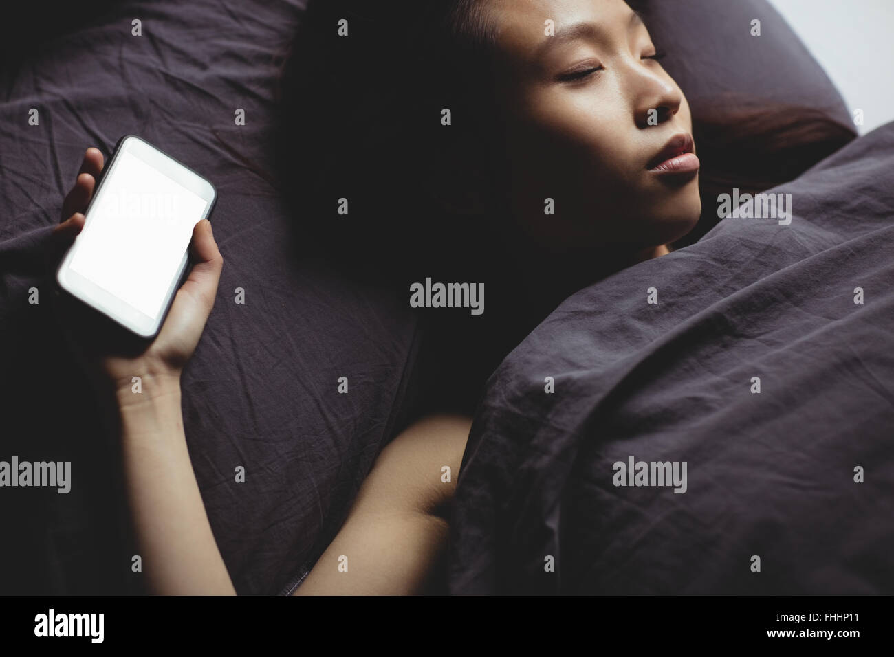 Brunette dormir sur le lit avec smartphone Banque D'Images